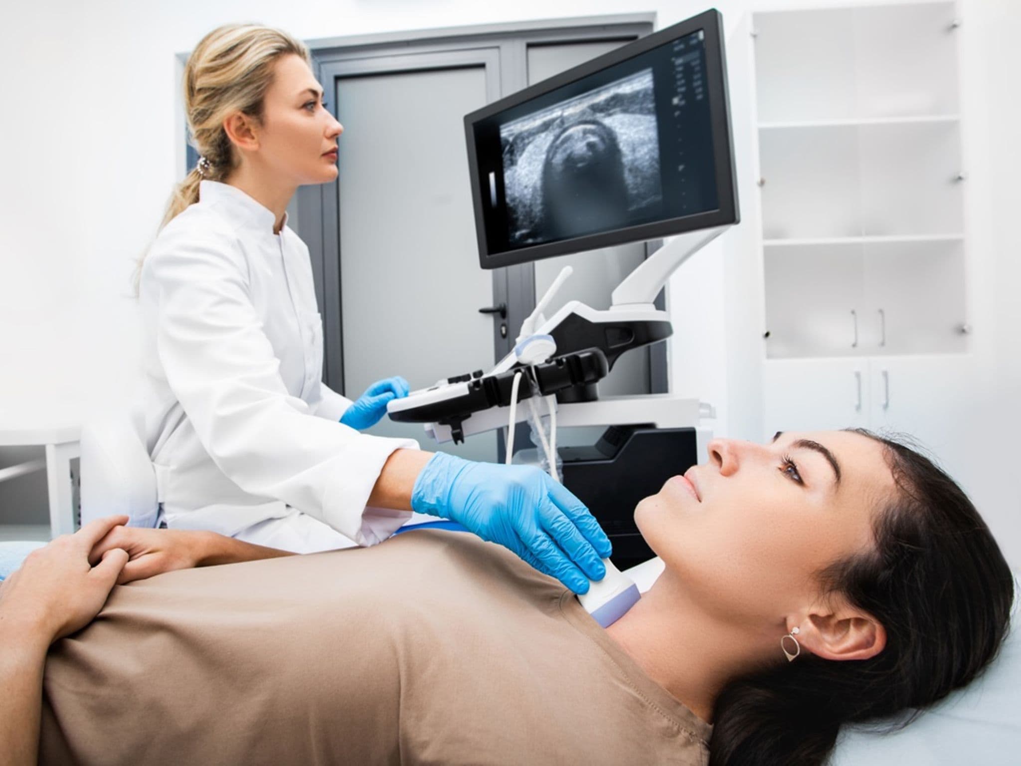 Junge Ärztin untersucht die Schilddrüse einer Patientin mit einem Ultraschall.