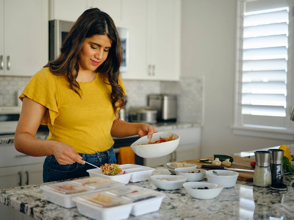 Meal Prep: Frau kocht vor und füllt Mahlzeiten in Tupperdosen ein.