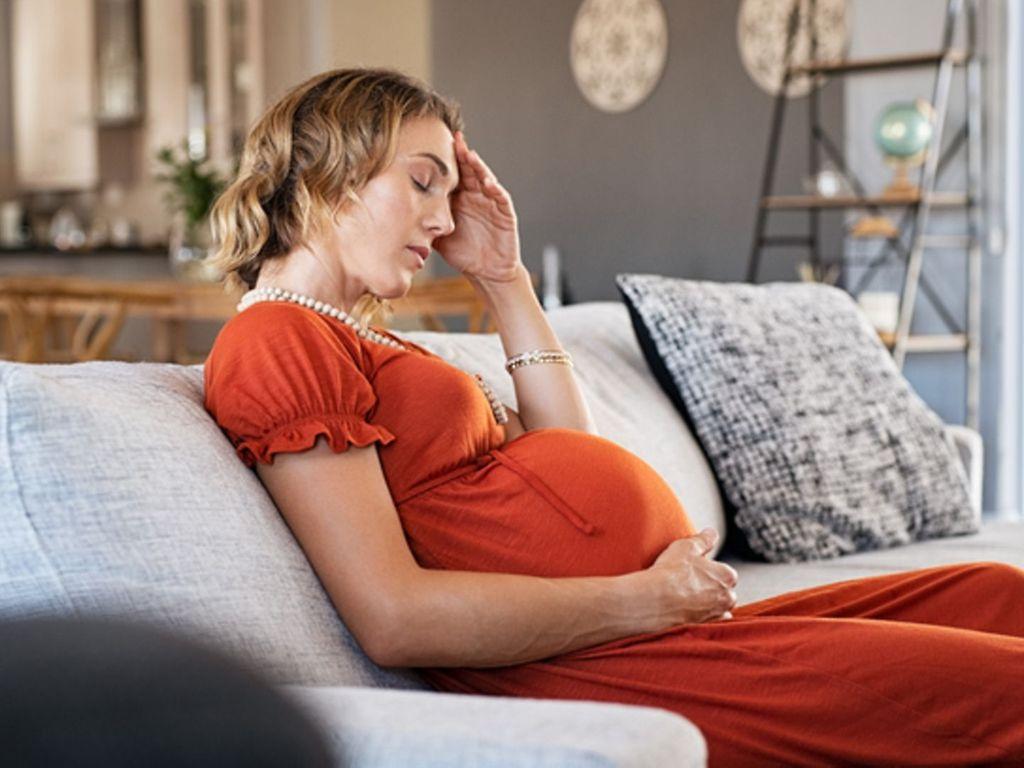 Hämorrhoiden in der Schwangerschaft: Schwangere sitzt erschöpft auf der Couch