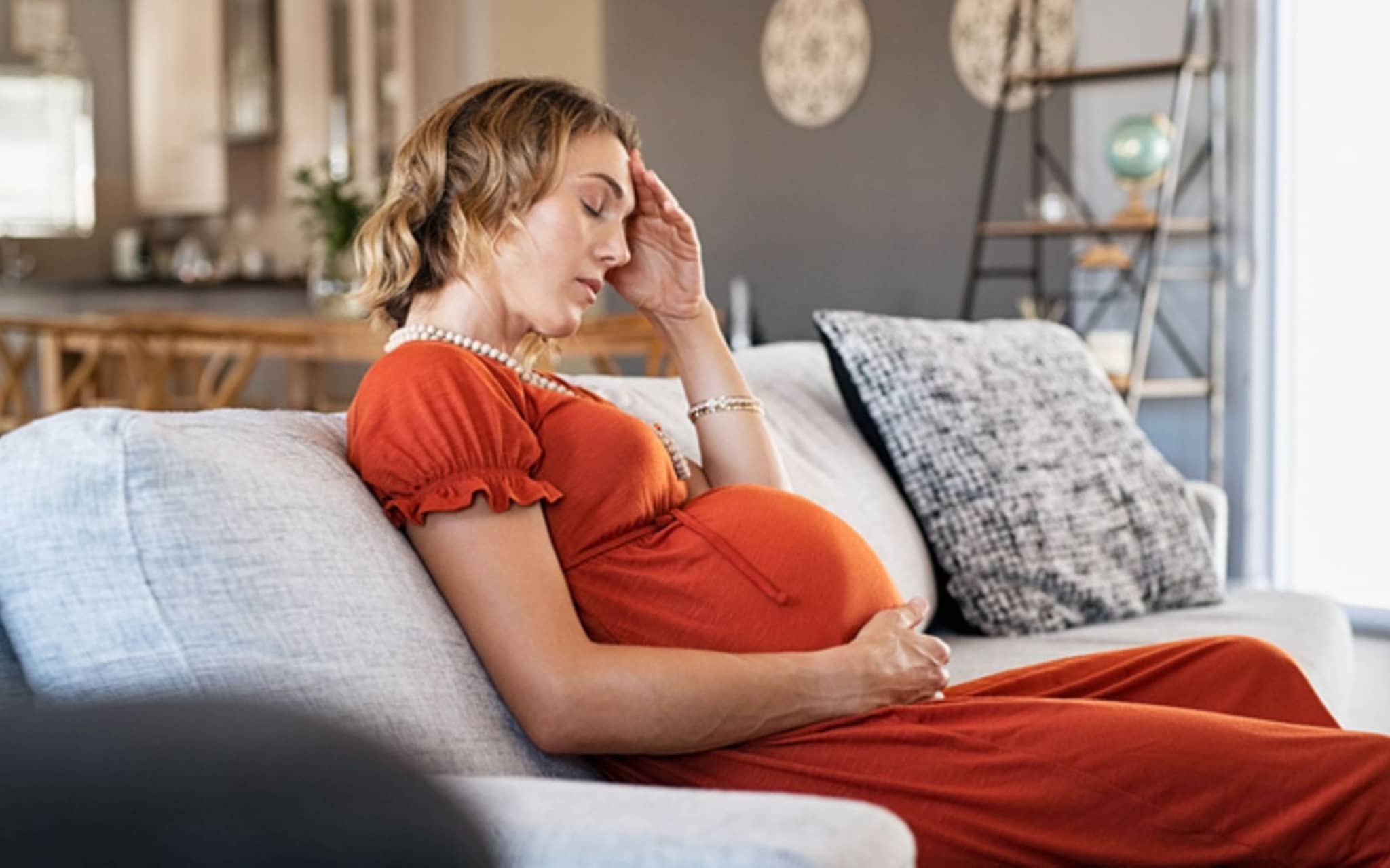 Hämorrhoiden in der Schwangerschaft: Schwangere sitzt erschöpft auf der Couch