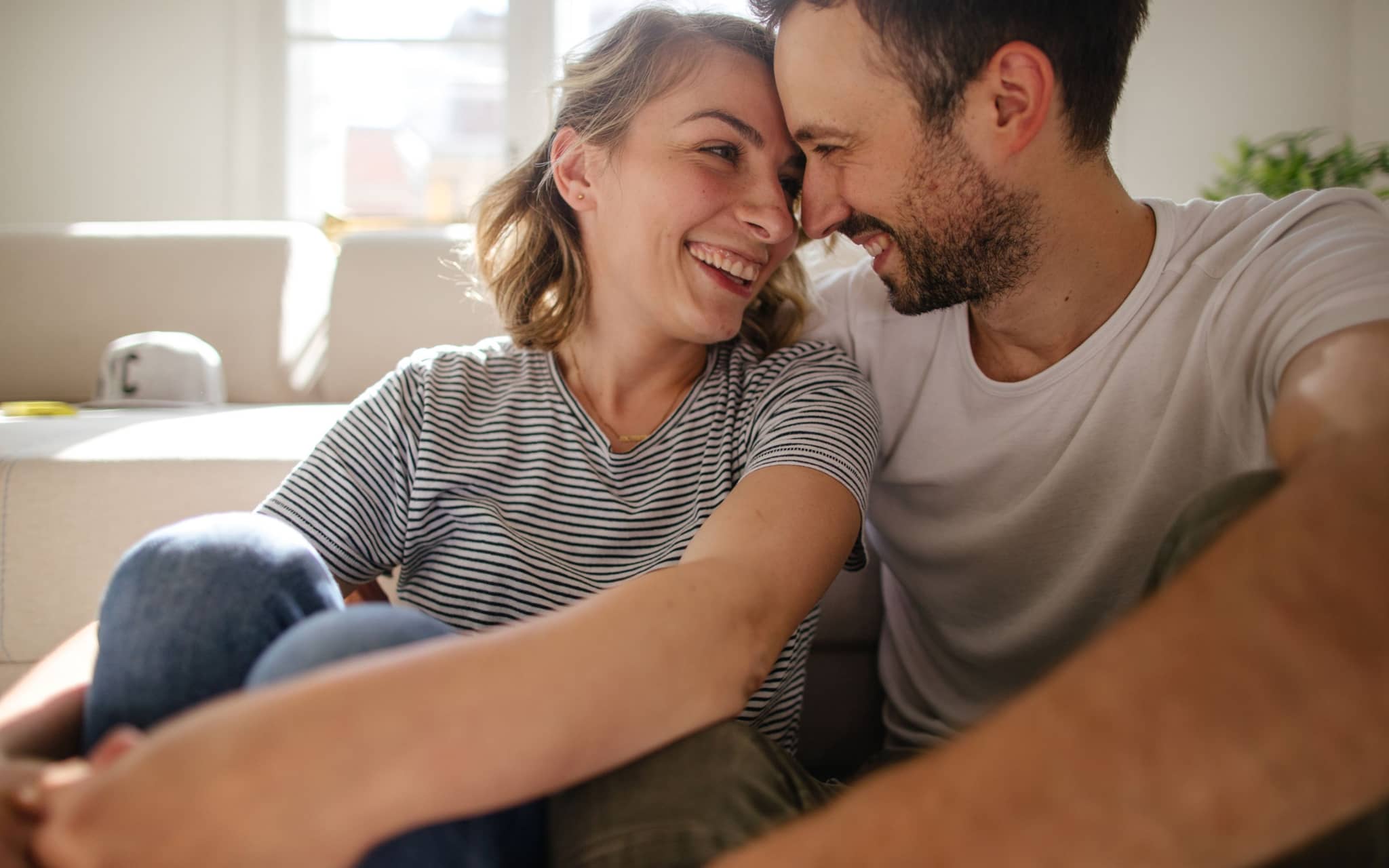 Cunnilingus: Eine junge Frau und ein junger Mann sitzen auf dem Fußboden im Schlafzimmer und sehen sich verliebt in die Augen.