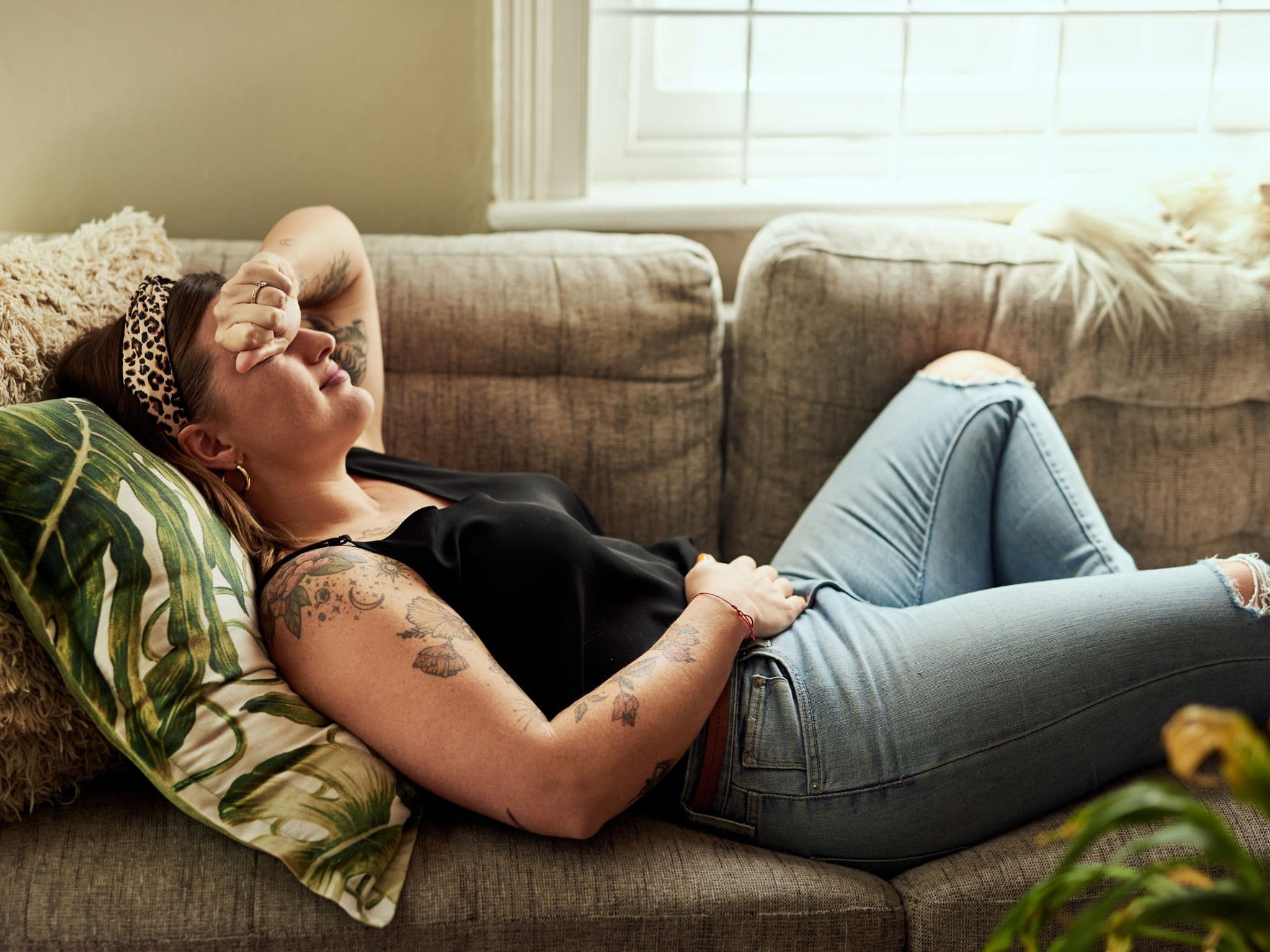 Vulvodynie: Junge Frau liegt betrübt im Bett und hält ihren Bauch fest.