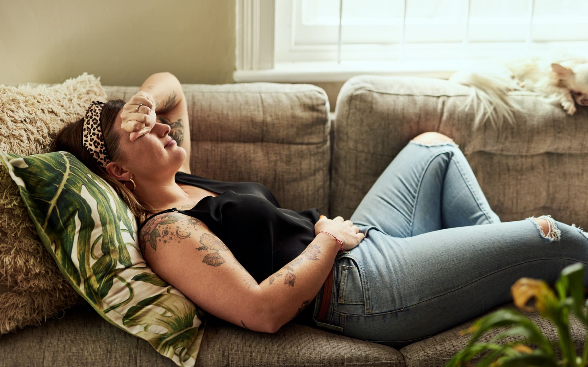 Vulvodynie: Junge Frau liegt betrübt im Bett und hält ihren Bauch fest.