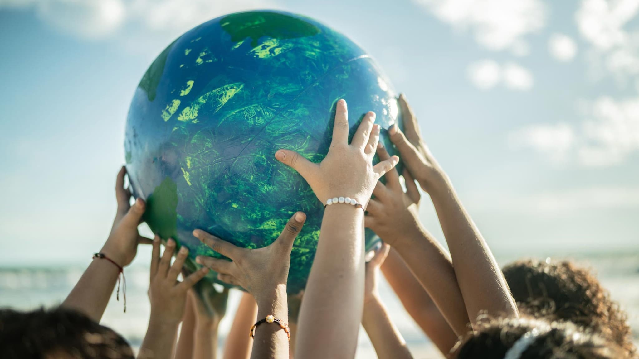 Nachhaltigkeit: Am Strand halten mehrere Kinder einen großen Ball nach oben, der an einen Planeten erinnert.