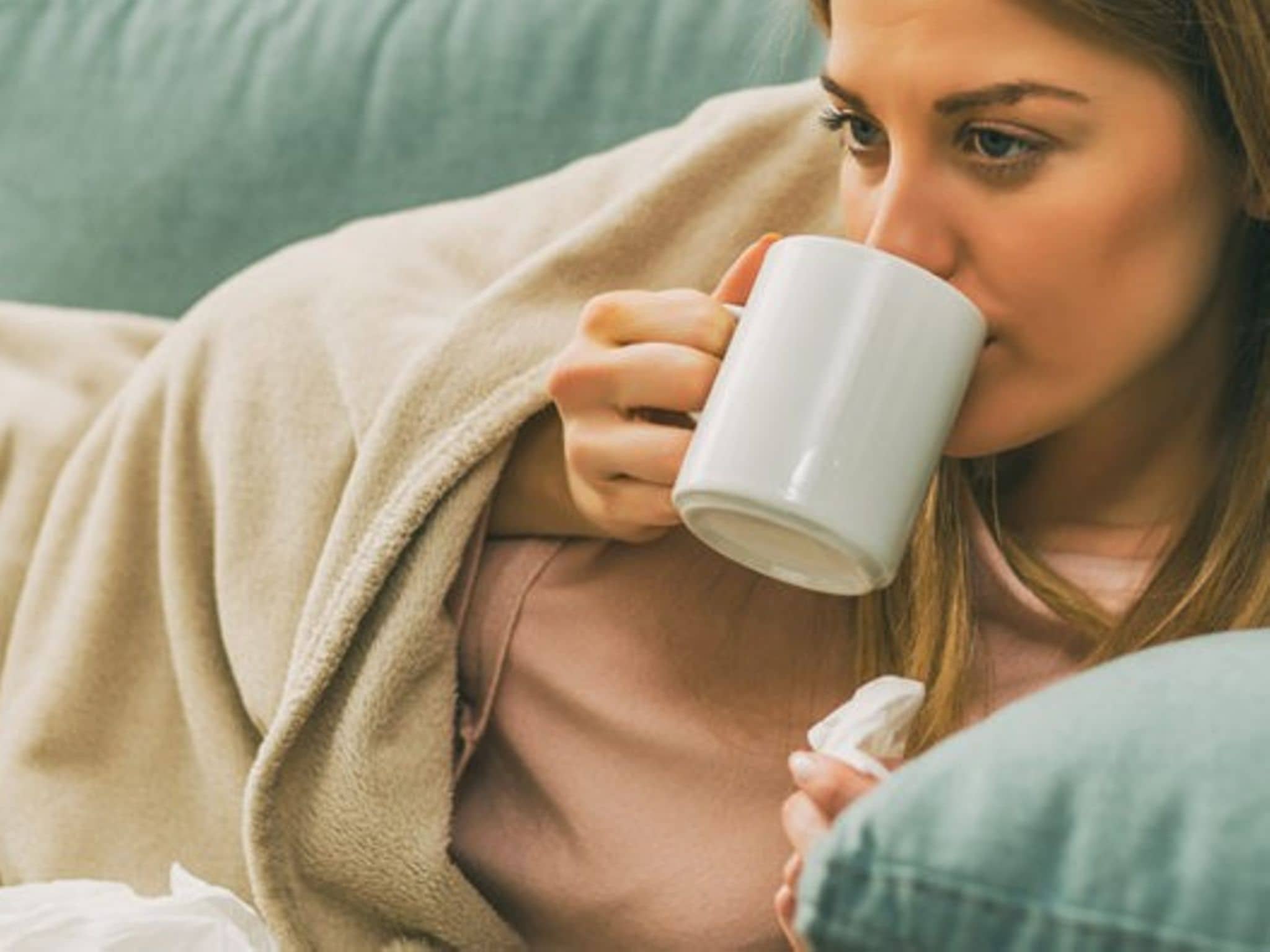 Erkältete Frau liegt auf dem Sofa und trinkt Tee