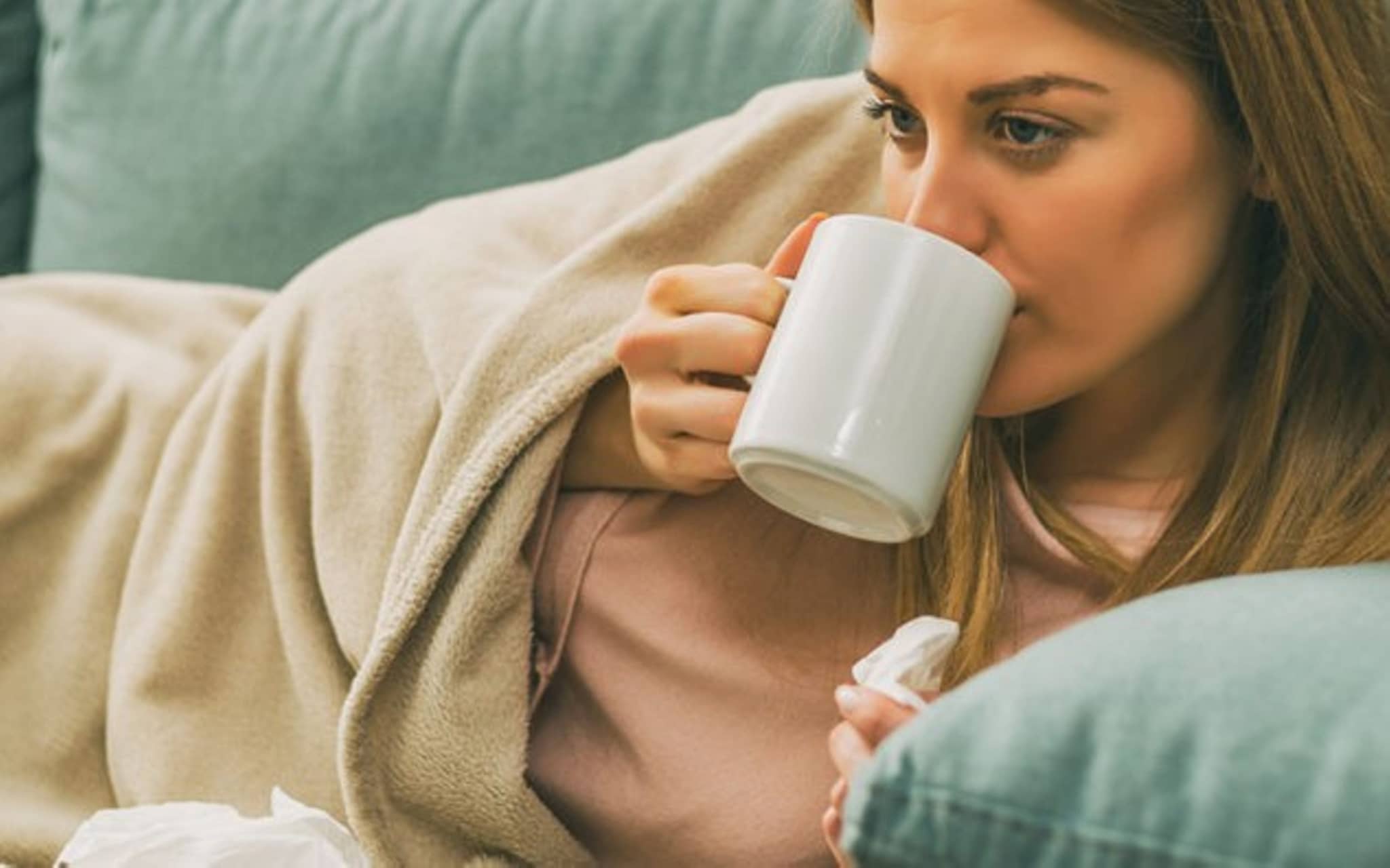 Erkältete Frau liegt auf dem Sofa und trinkt Tee