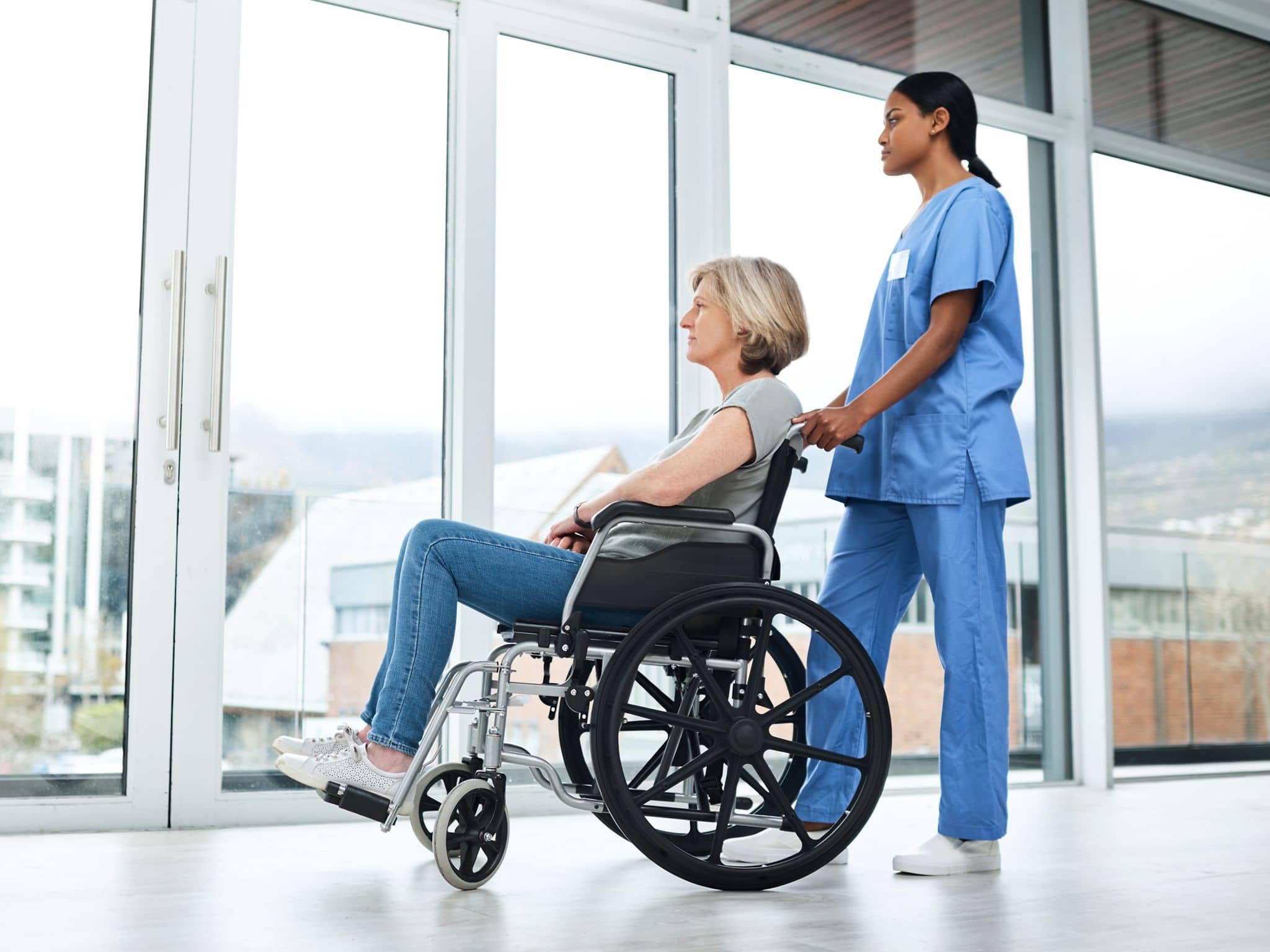 Frau wird im Rollstuhl von einer Krankenpflegerin aus dem Krankenhaus entlassen.