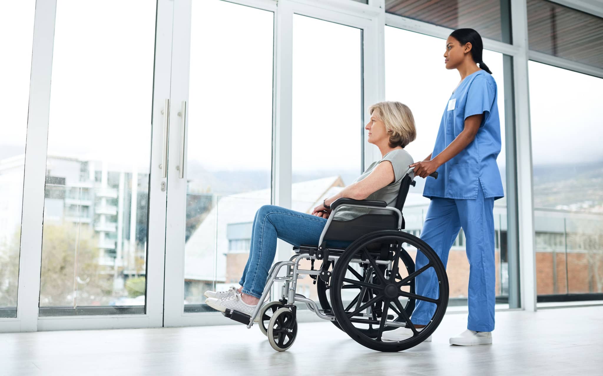 Frau wird im Rollstuhl von einer Krankenpflegerin aus dem Krankenhaus entlassen.