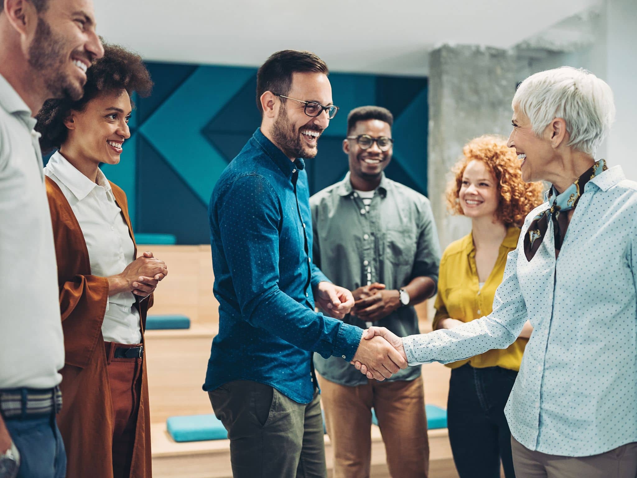 Wechseljahre im Job: Eine ältere Frau gratuliert einem Mann aus ihrem Team per Handschlag
