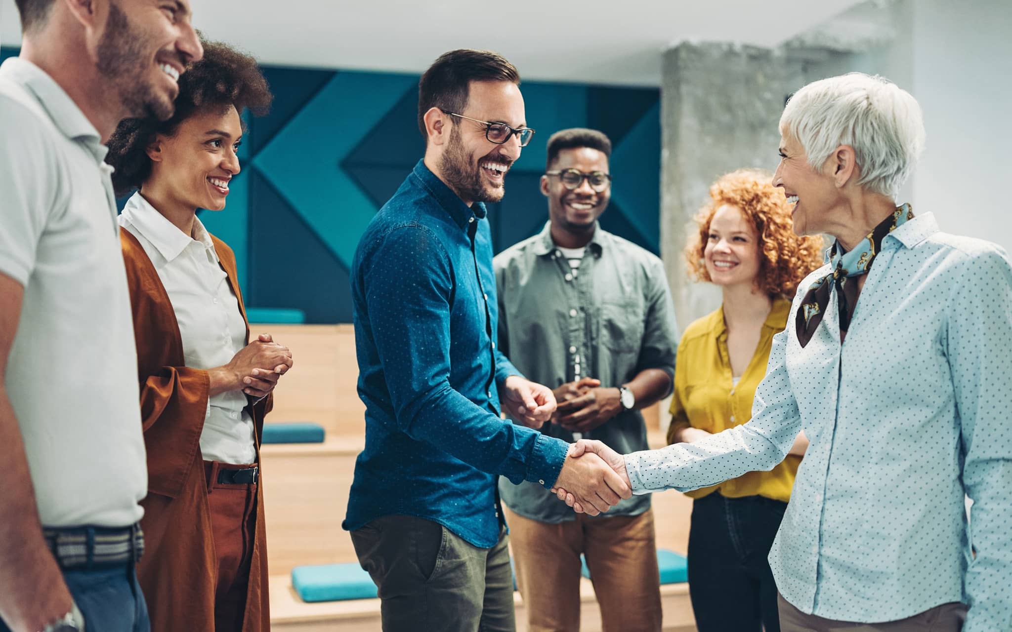 Wechseljahre im Job: Eine ältere Frau gratuliert einem Mann aus ihrem Team per Handschlag