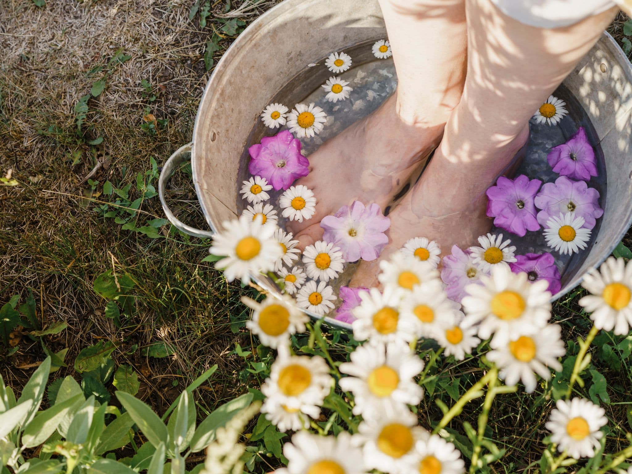 Eine Frau gönnt sich ein Fußbad mit Blüten. Zu sehen sind lediglich ihre Füße.