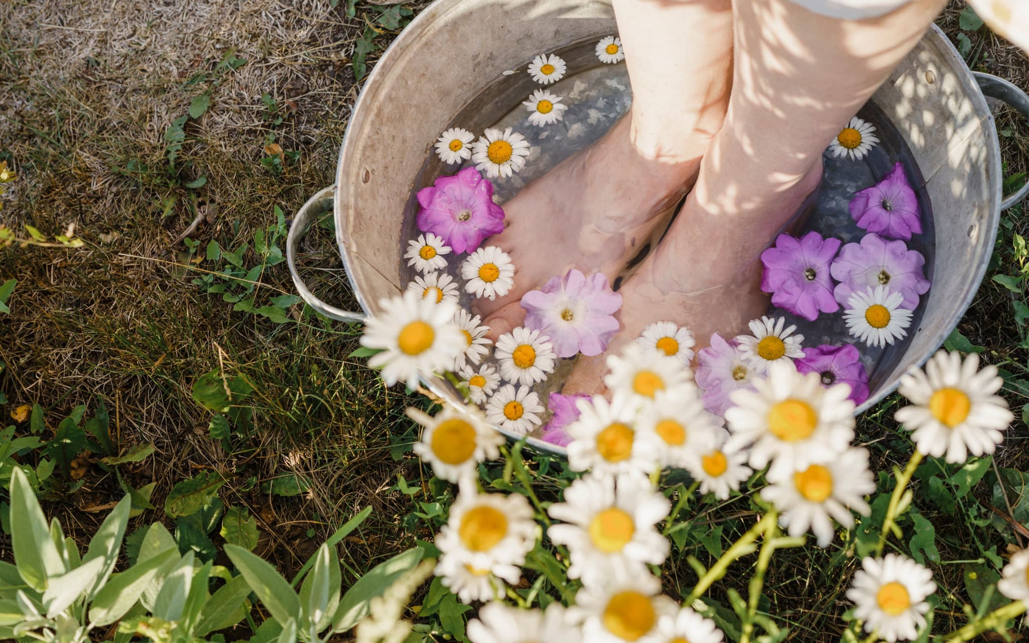 Eine Frau gönnt sich ein Fußbad mit Blüten. Zu sehen sind lediglich ihre Füße.