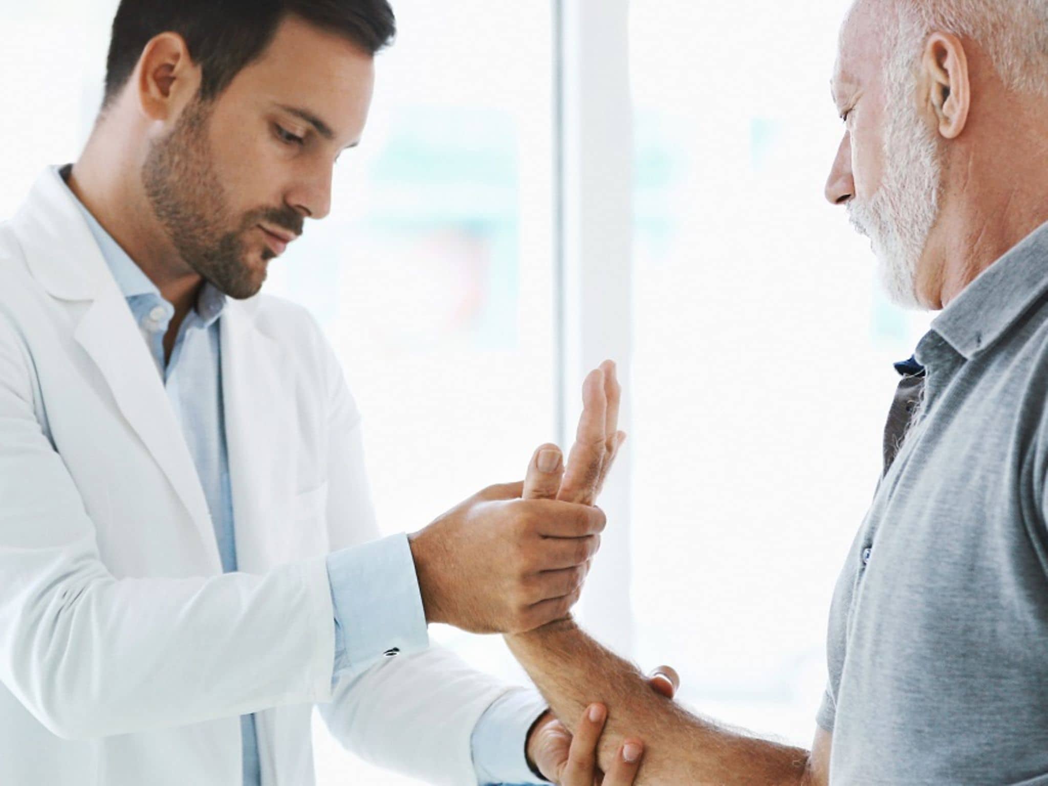 Mann mit Rheuma beim Arzt: Finger und Handgelenk werden untersucht.
