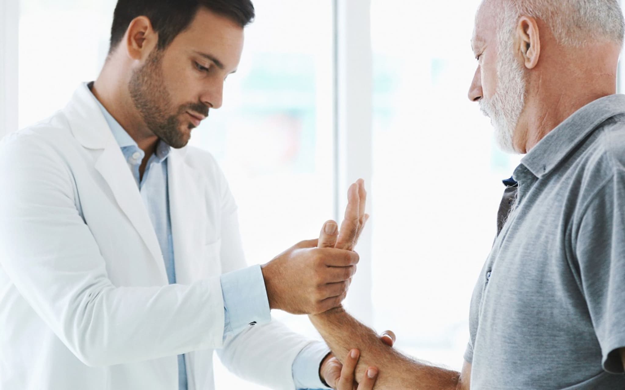 Mann mit Rheuma beim Arzt: Finger und Handgelenk werden untersucht.