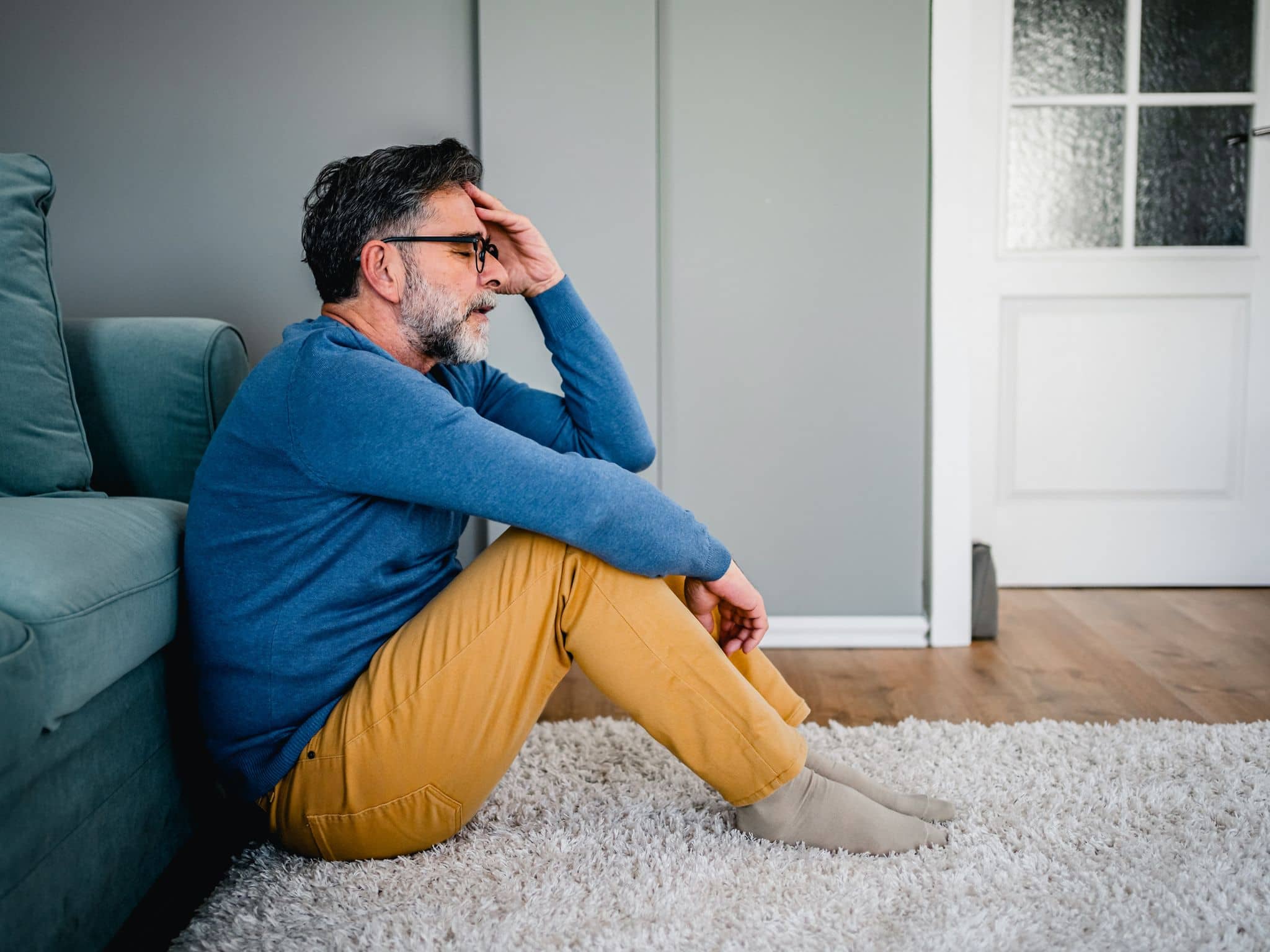 PanMann sitzt vor auf dem Fußboden vor einem Sofa und hält seinen Kopf
