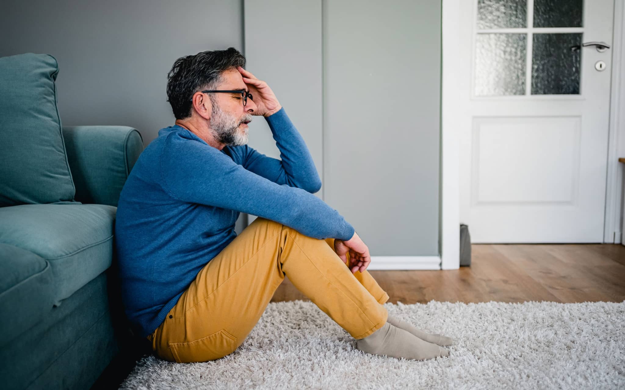 PanMann sitzt vor auf dem Fußboden vor einem Sofa und hält seinen Kopf