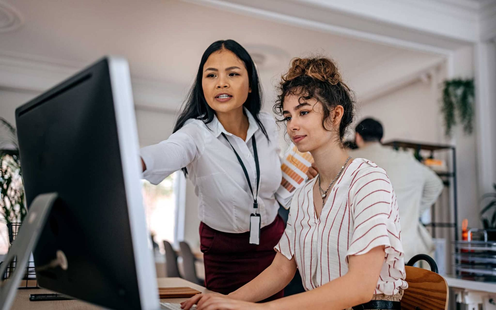 Zwei Kolleginnen sind im Gespräch und gucken auf einen Bildschirm