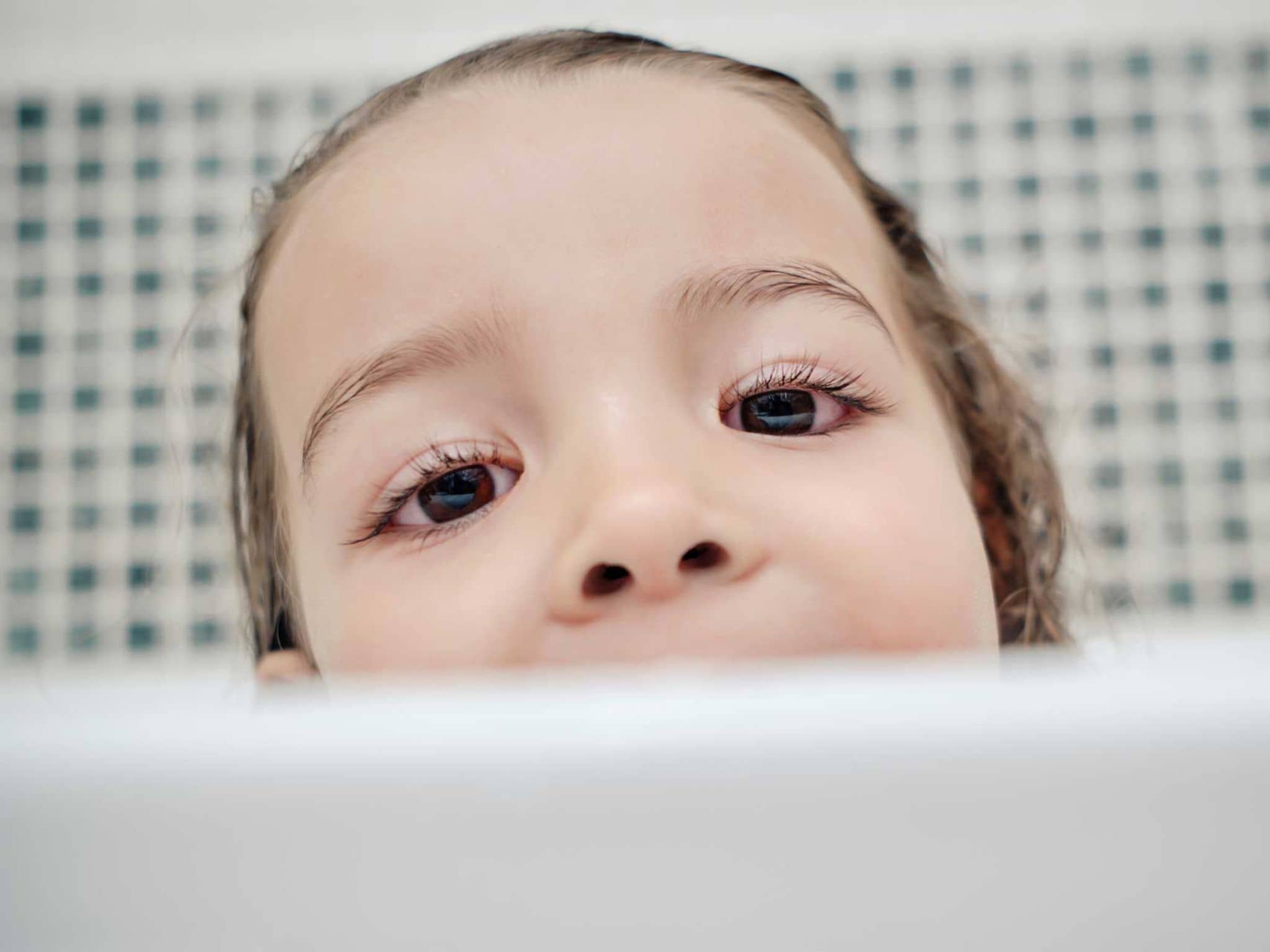 Kind mit Bindehautentzündung guckt über Badewannenrand