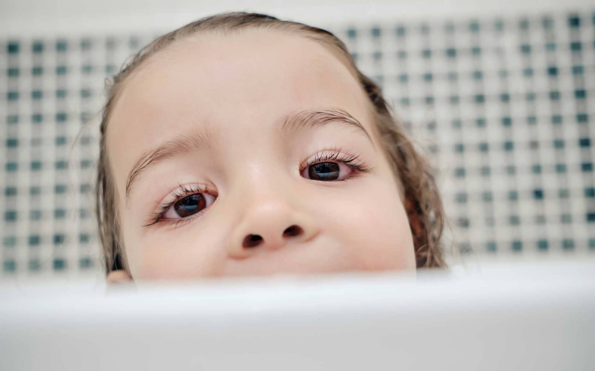 Kind mit Bindehautentzündung guckt über Badewannenrand