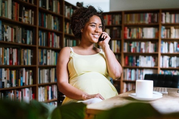 Exklusive Schwangerenberatung: Schwangere Frau sitzt auf der Couch und telefoniert.