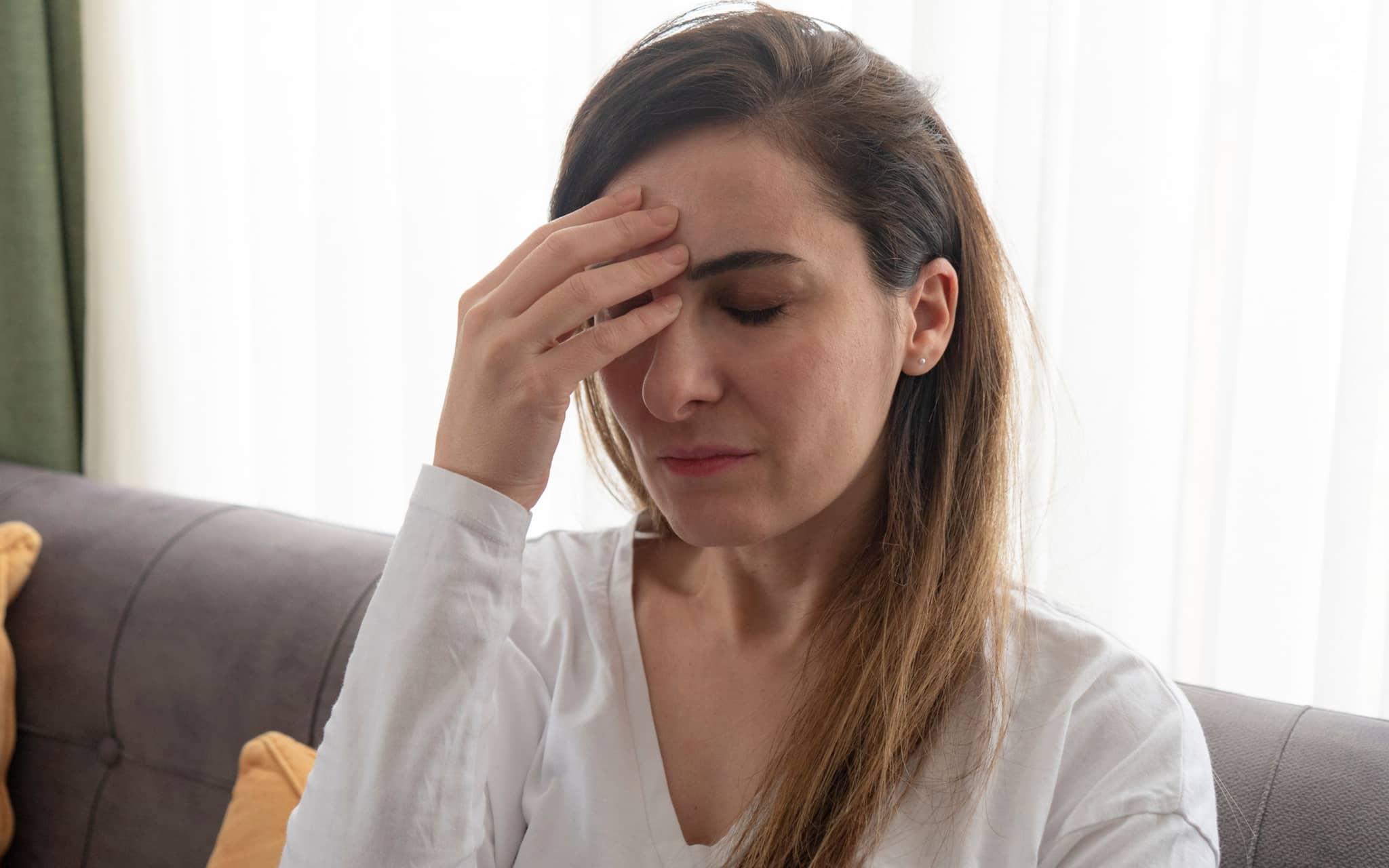 Eine Frau erleidet eine Migräneattacke und greift sich an den Kopf.