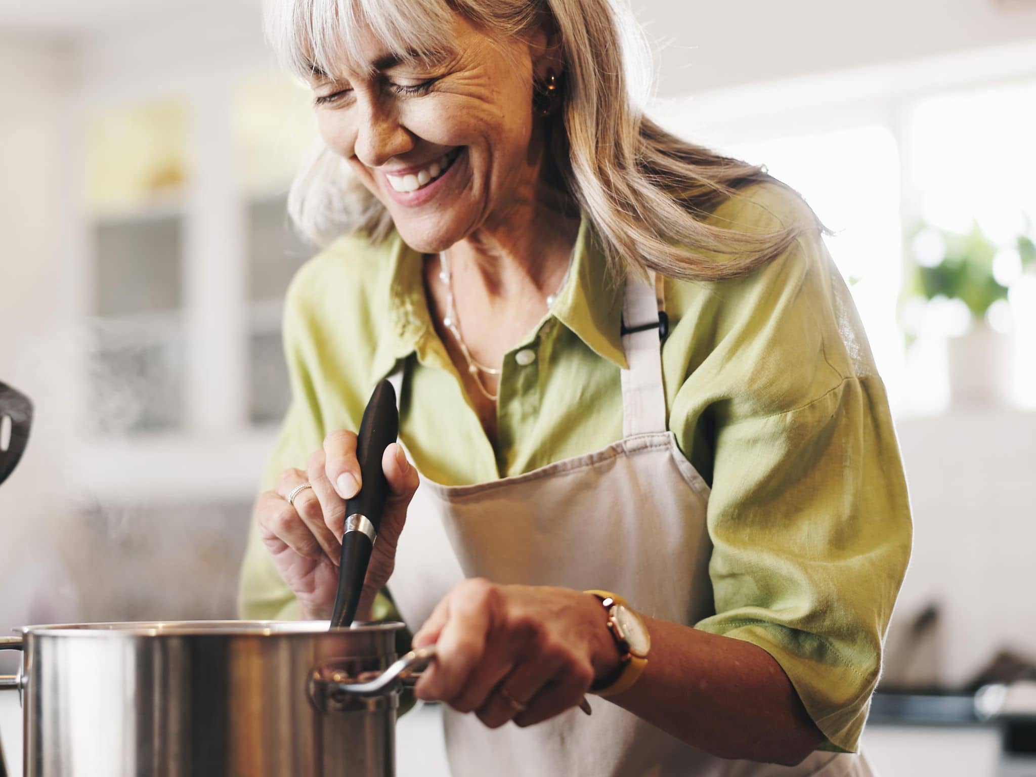Rezept für gebratenen Weißkohl: Ältere Frau macht gebratenen Weißkohl mit Kabanossi in einem Topf.
