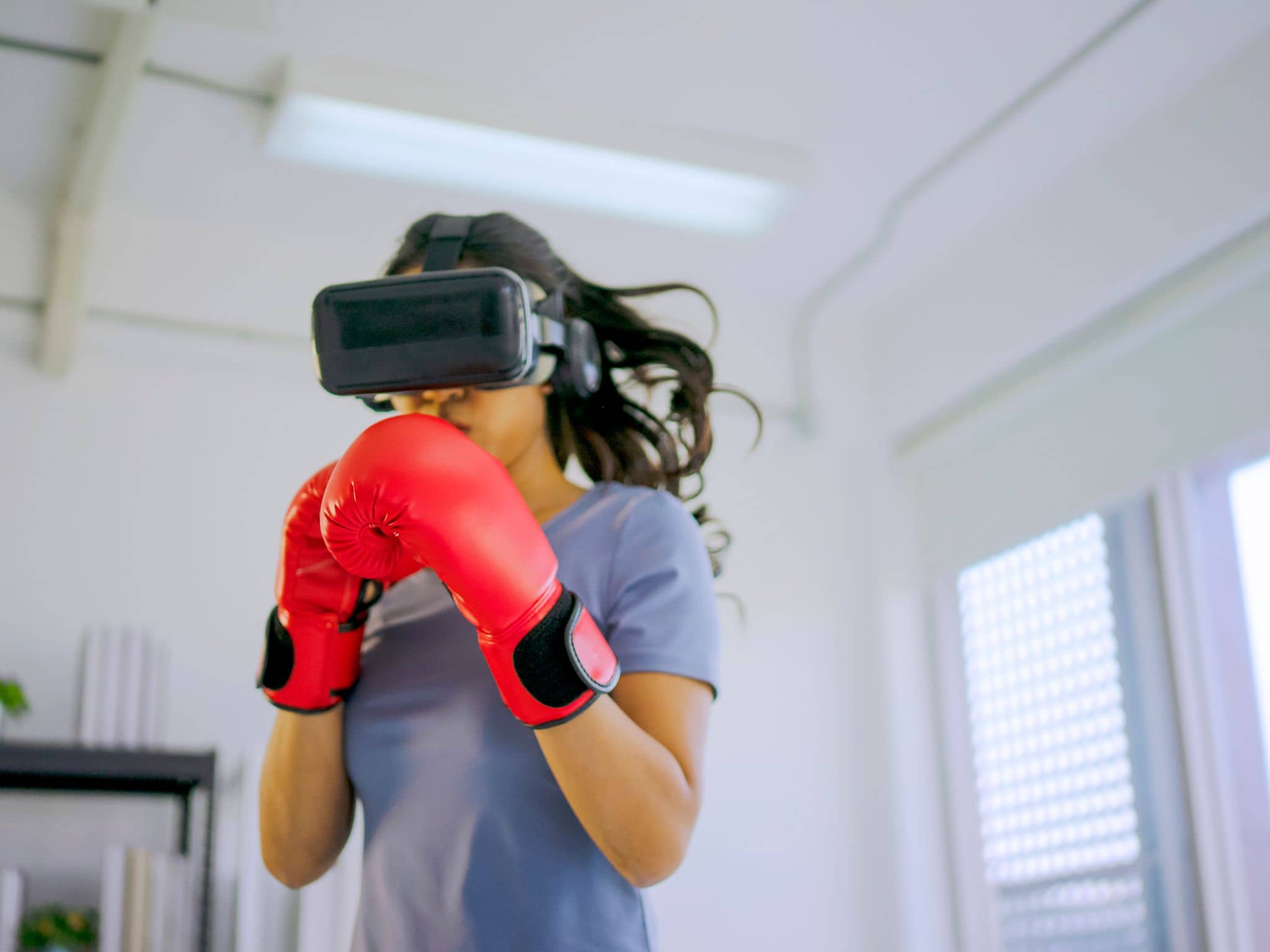 Eine Frau boxt mit einer VR-Brille und macht so VR-Sport.