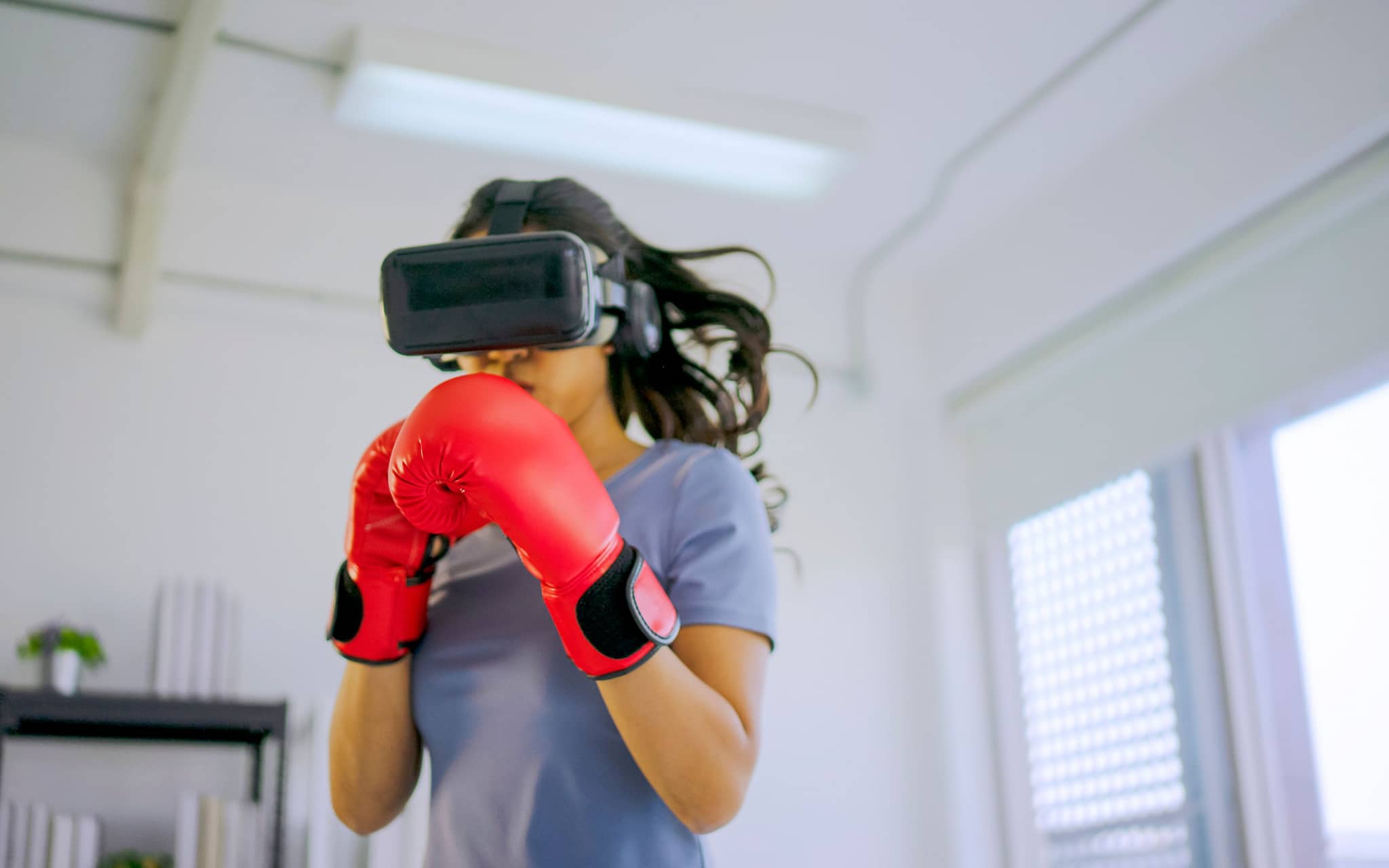 Eine Frau boxt mit einer VR-Brille und macht so VR-Sport.
