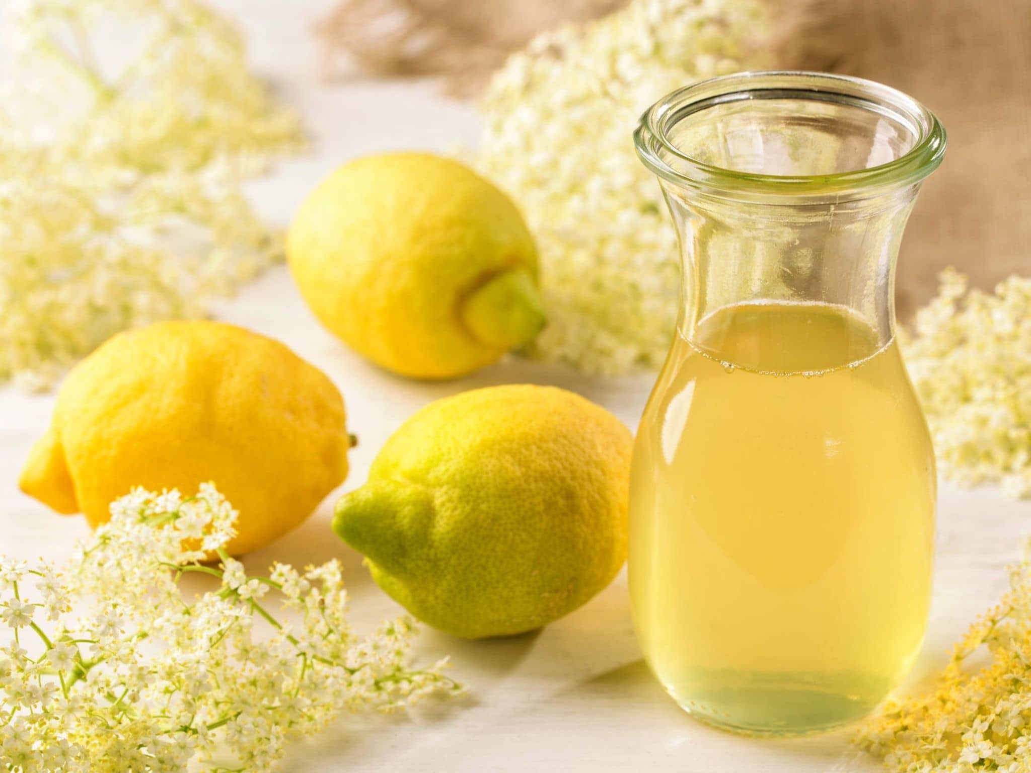 Frisch gemachter Holunderblütensirup neben den Zutaten Holunderblüten und Zitronen.