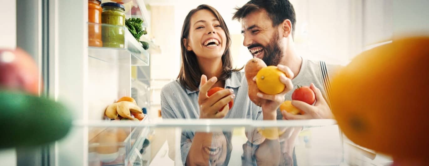 Paar holt freudig ein paar Lebensmittel aus einem Kühlschrank