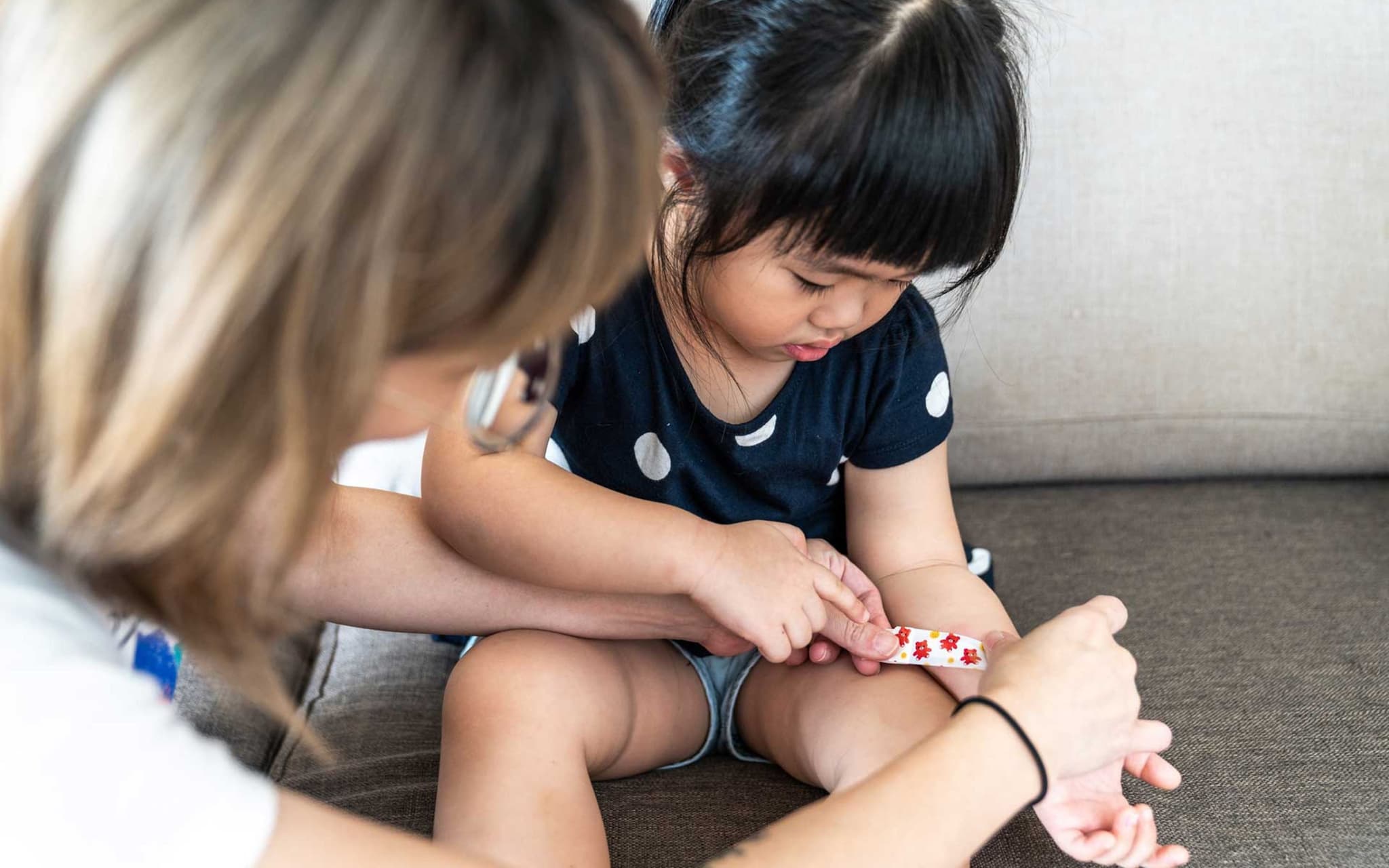 Mutter legt bei kleinem Mädchen ein Pflaster an