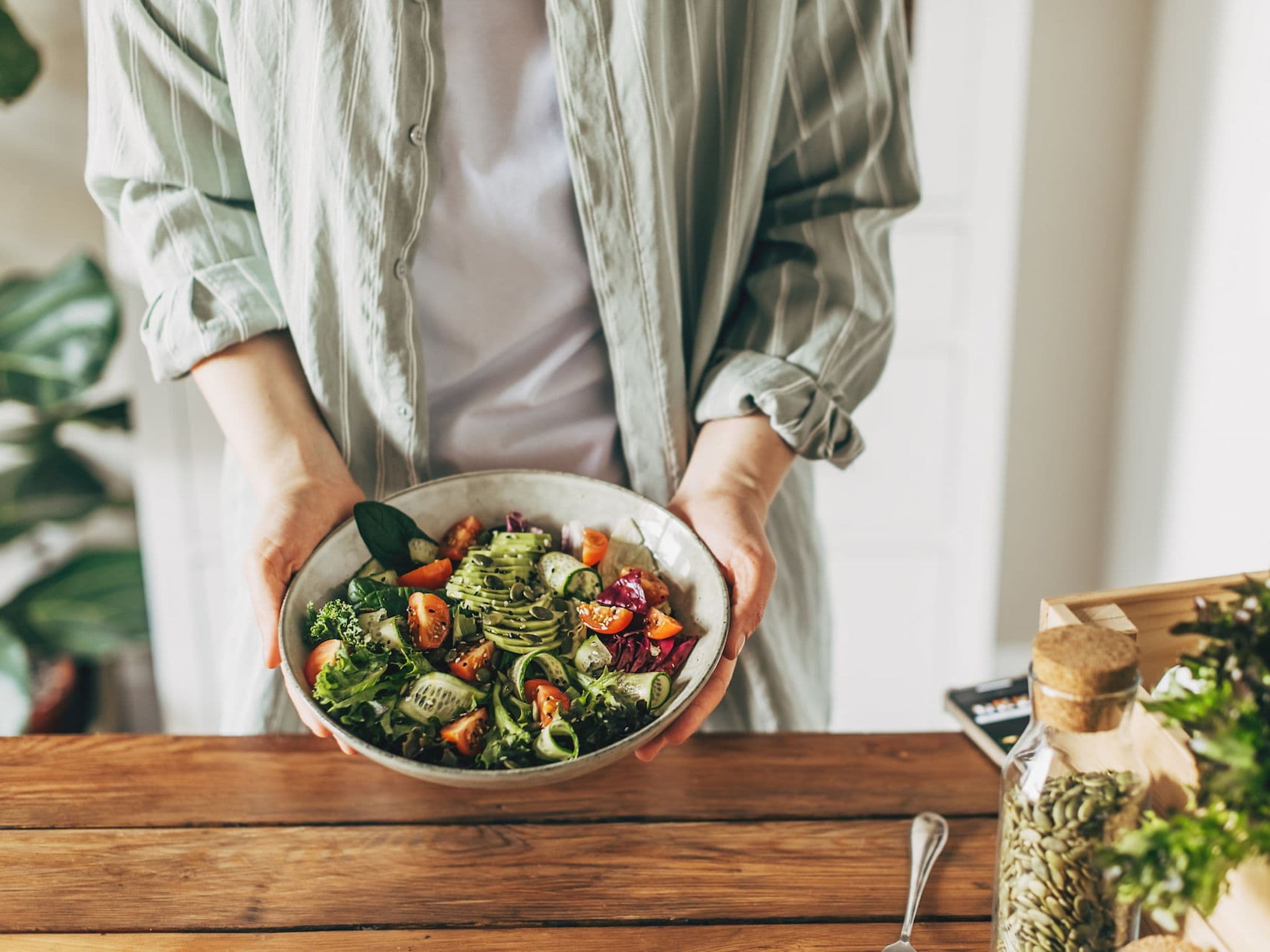 Paleo: Frau hält Schüssel mit Salat mit Gurke, Tomaten, Kürbiskernen