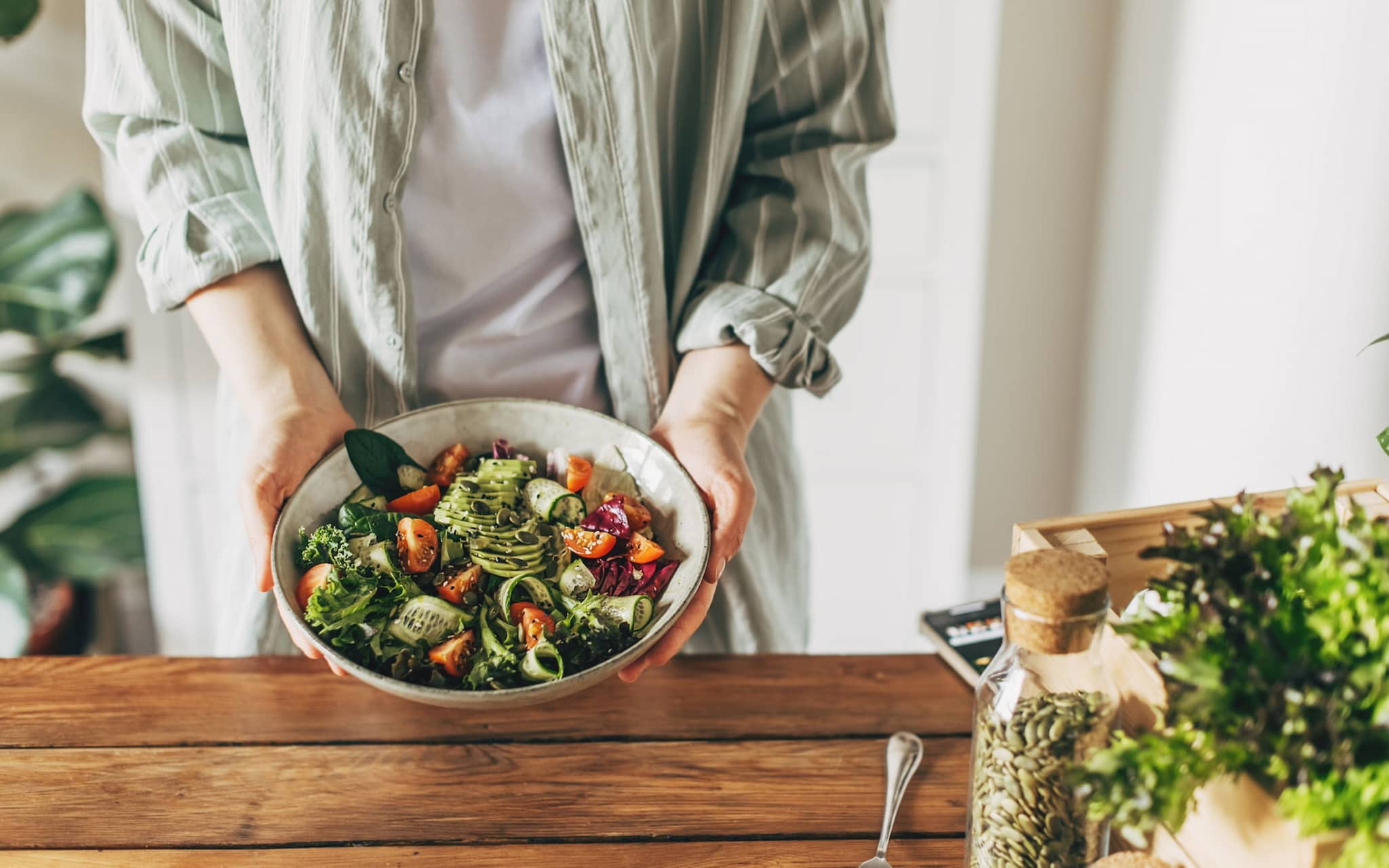 Paleo: Frau hält Schüssel mit Salat mit Gurke, Tomaten, Kürbiskernen