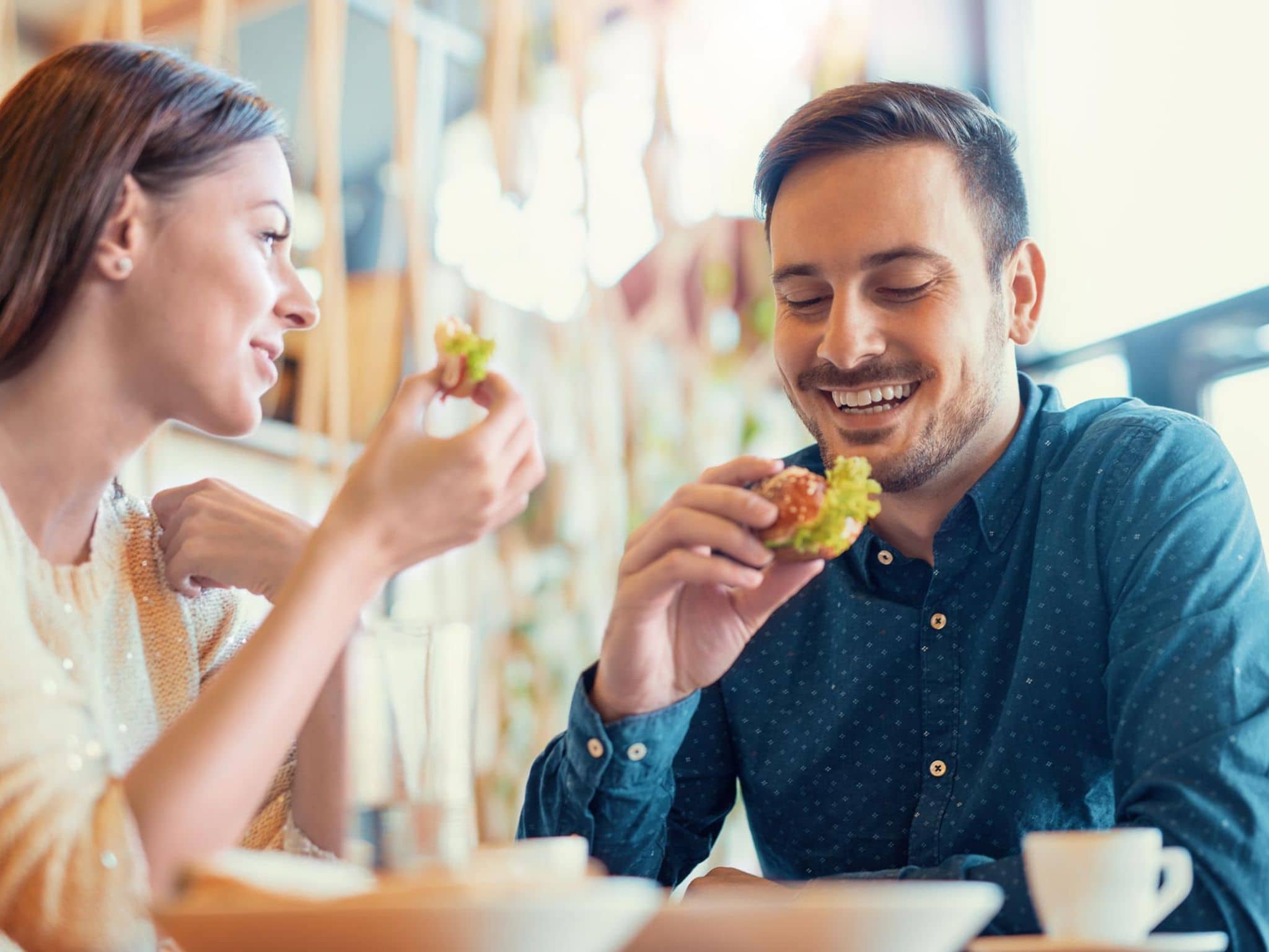 Ernährungsmythen: Junges Paar sitzt in der Küche und isst Brötchen mit frischem Salat.
