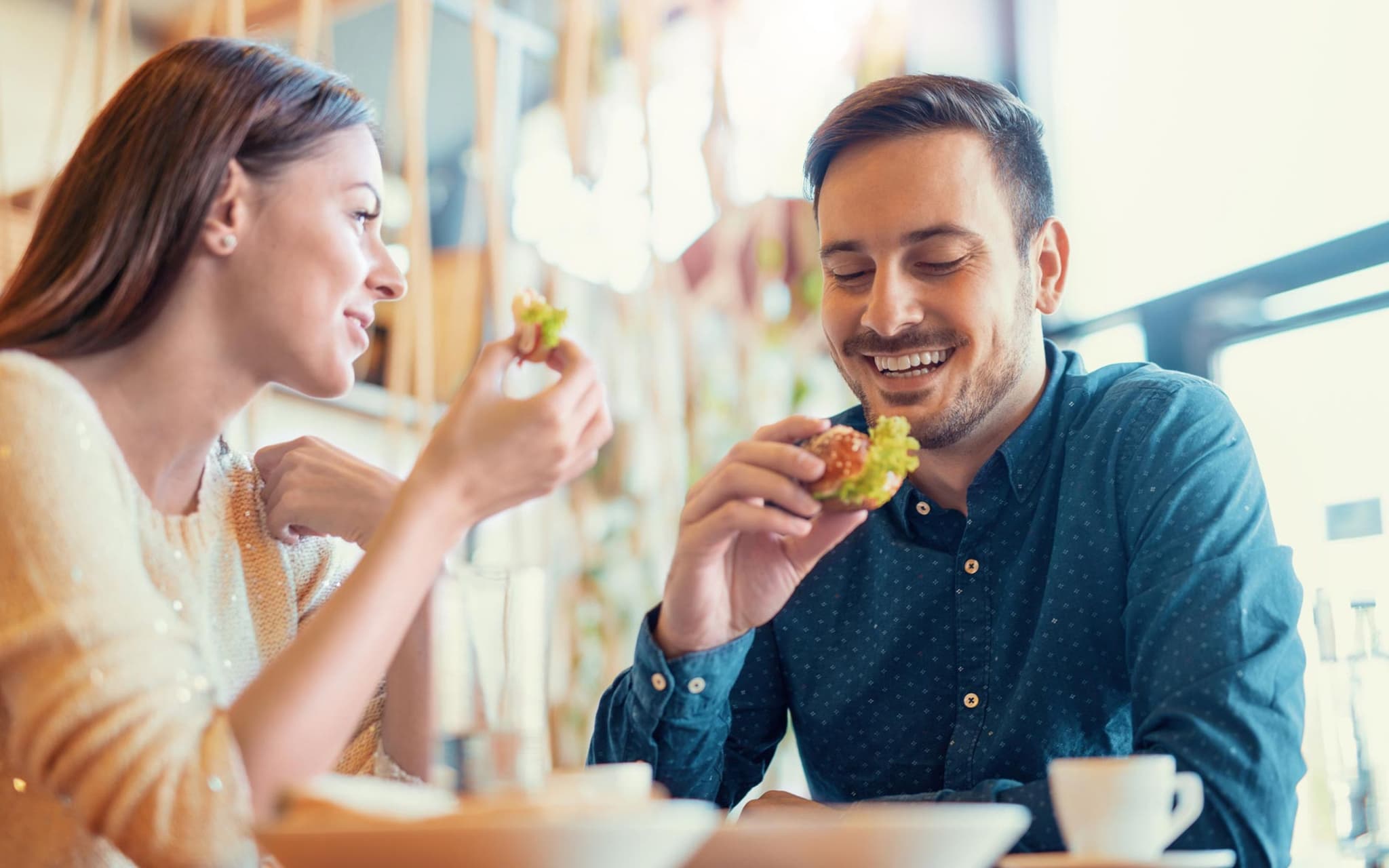 Ernährungsmythen: Junges Paar sitzt in der Küche und isst Brötchen mit frischem Salat.