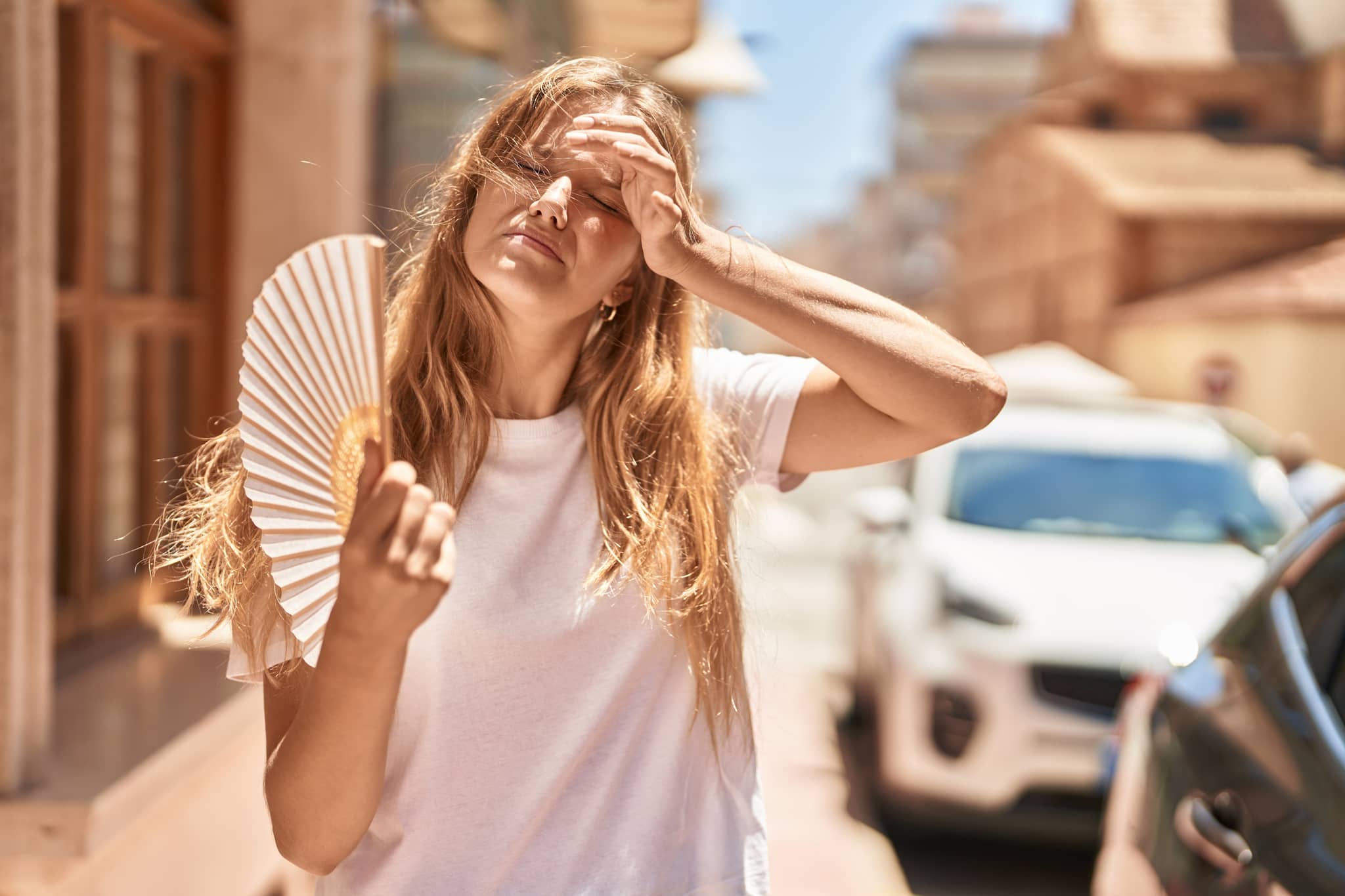 Junges blondes Mädchen benutzt Handfächer auf der Straße