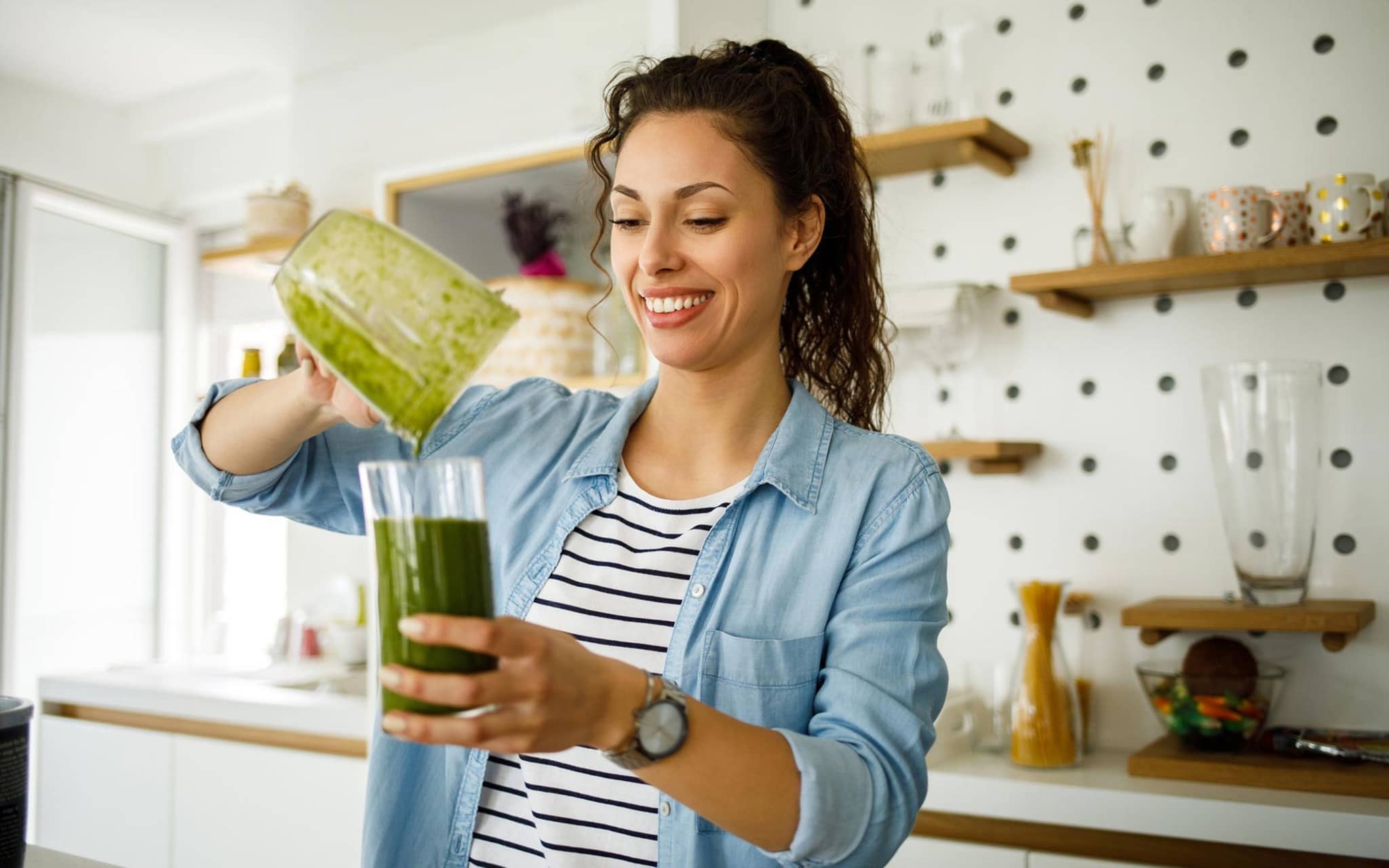Gesunder Grünkohl: Junge Frau bereitet sich in ihrer Küche einen Grünkohl-Smoothie zu.