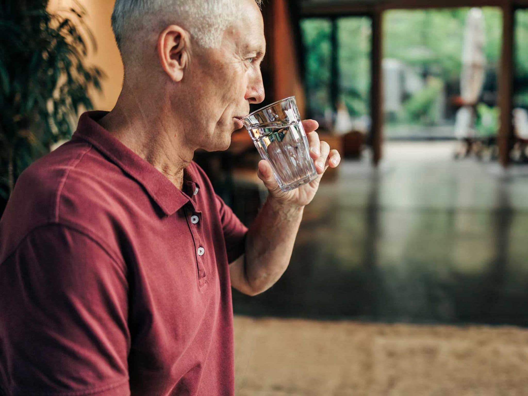 Älterer Mann im roten Poloshirt trinkt ein Glas Wasser