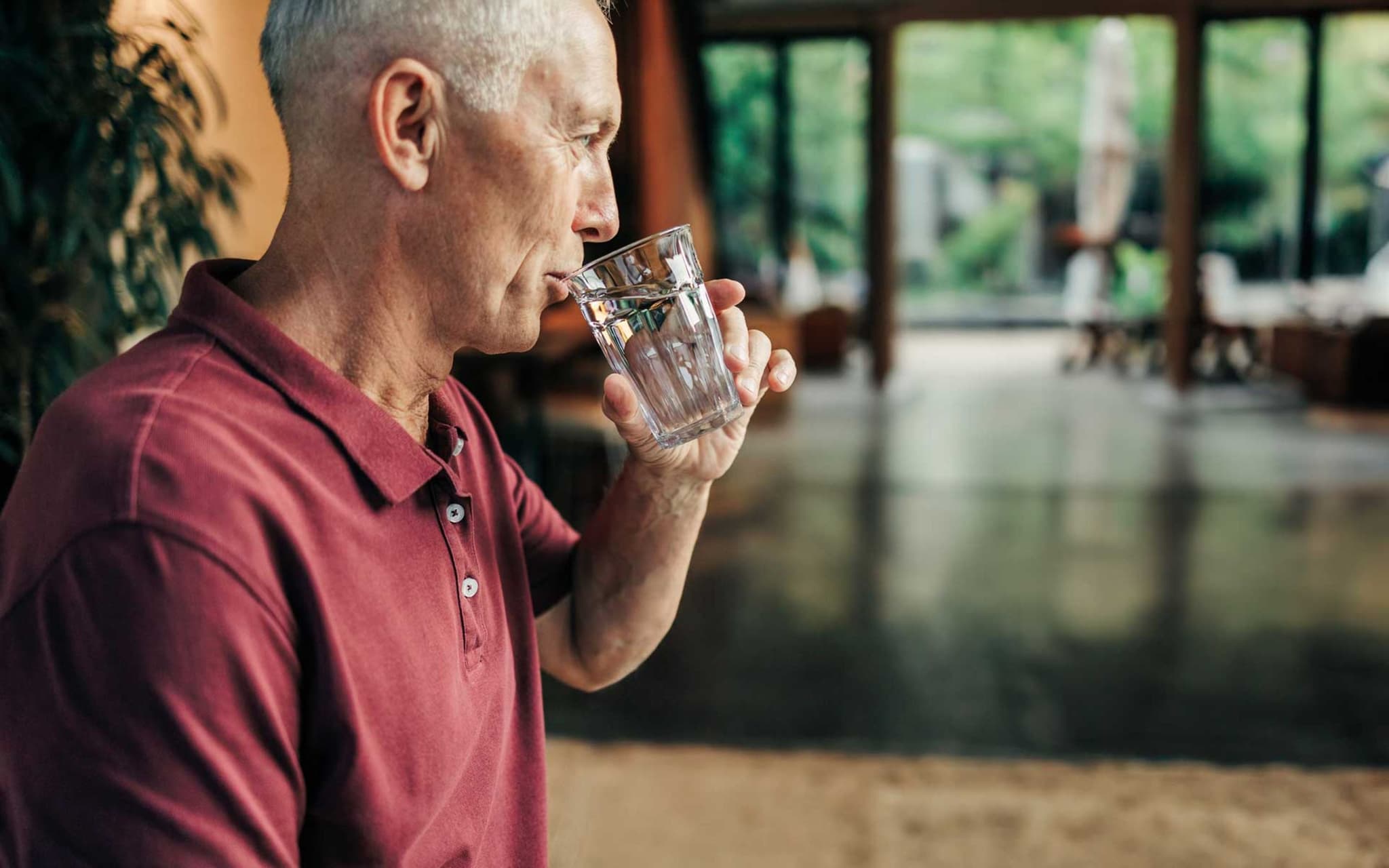 Älterer Mann im roten Poloshirt trinkt ein Glas Wasser
