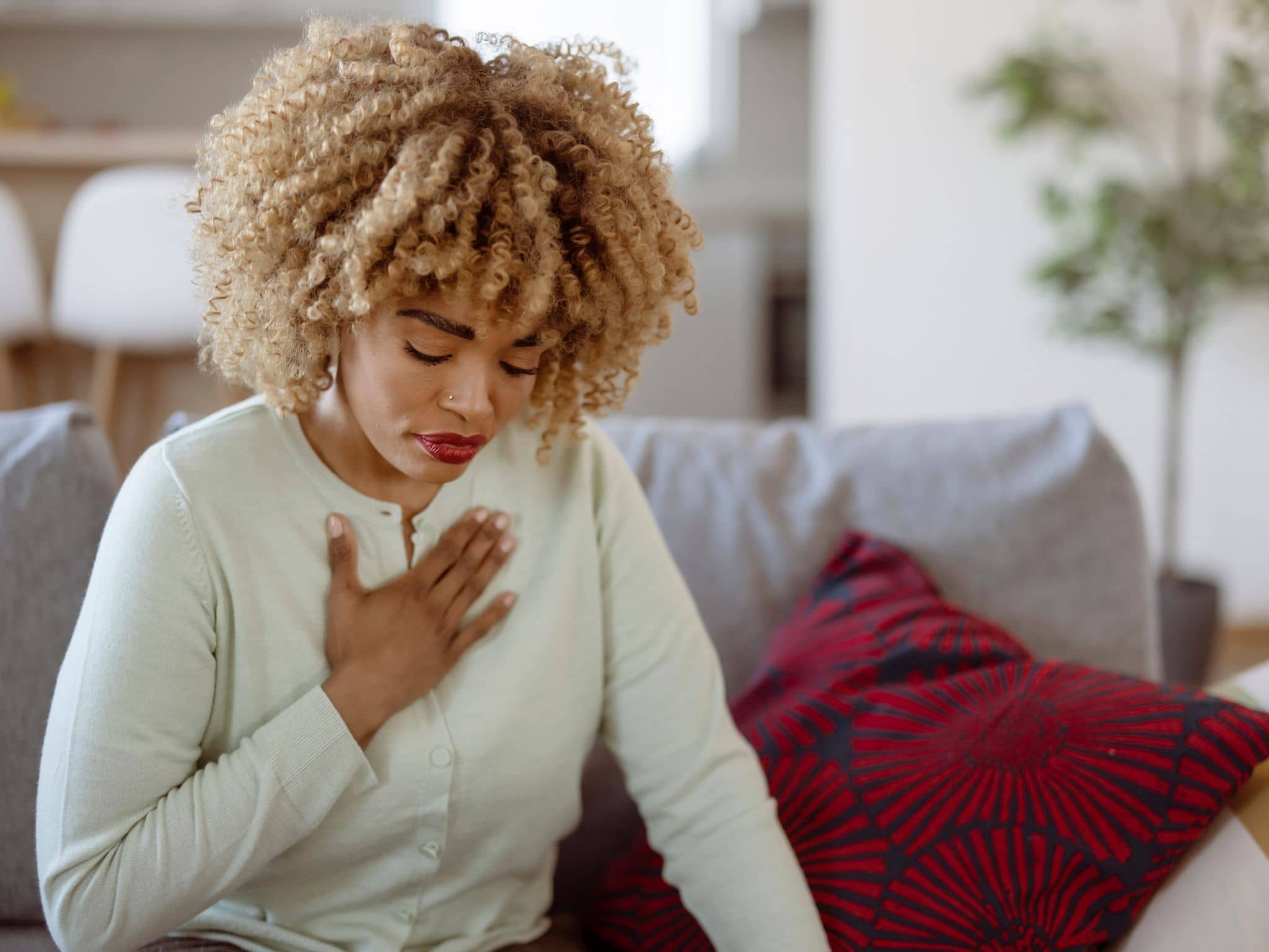 Herzinfarkt bei Frauen: Eine schwarze Frau sitzt auf einem Sofa und hält sich die Hand an die Brust