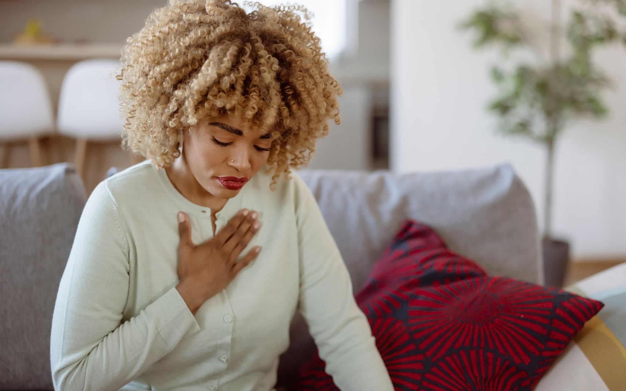 Herzinfarkt bei Frauen: Eine schwarze Frau sitzt auf einem Sofa und hält sich die Hand an die Brust