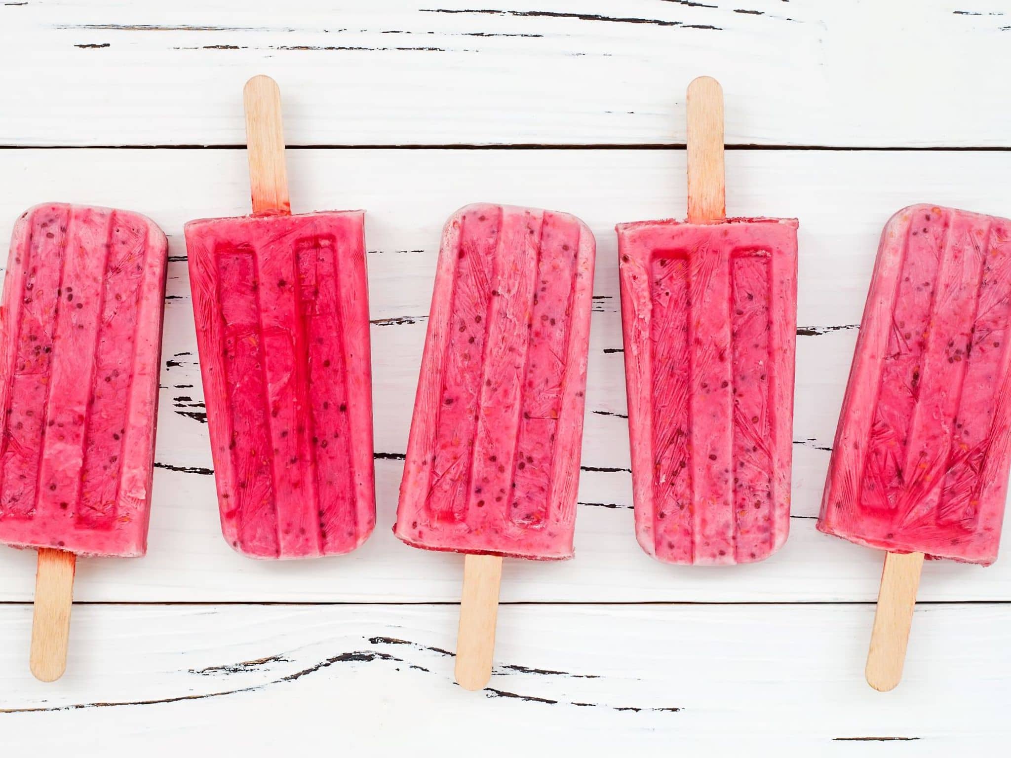 Fünf Eis am Stiel liegen auf einem Brett.