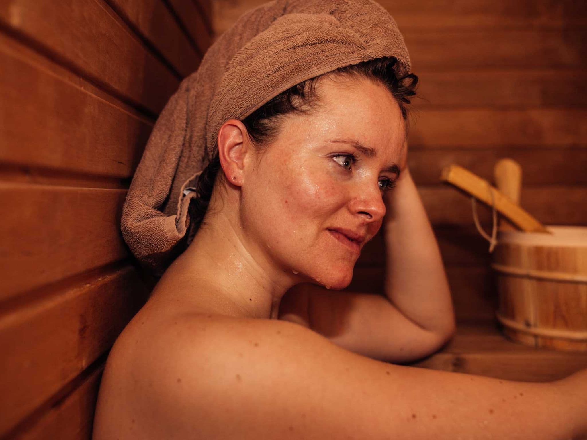 Frau hat ein Handtuch ums Haar gewickelt und schwitzt in Sauna