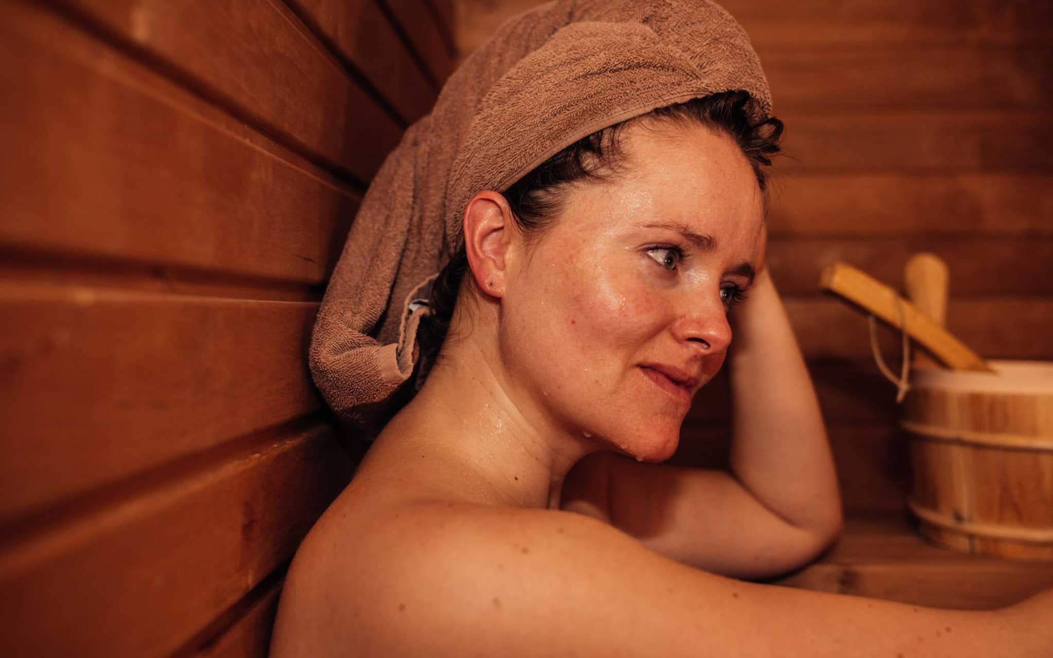 Frau hat ein Handtuch ums Haar gewickelt und schwitzt in Sauna