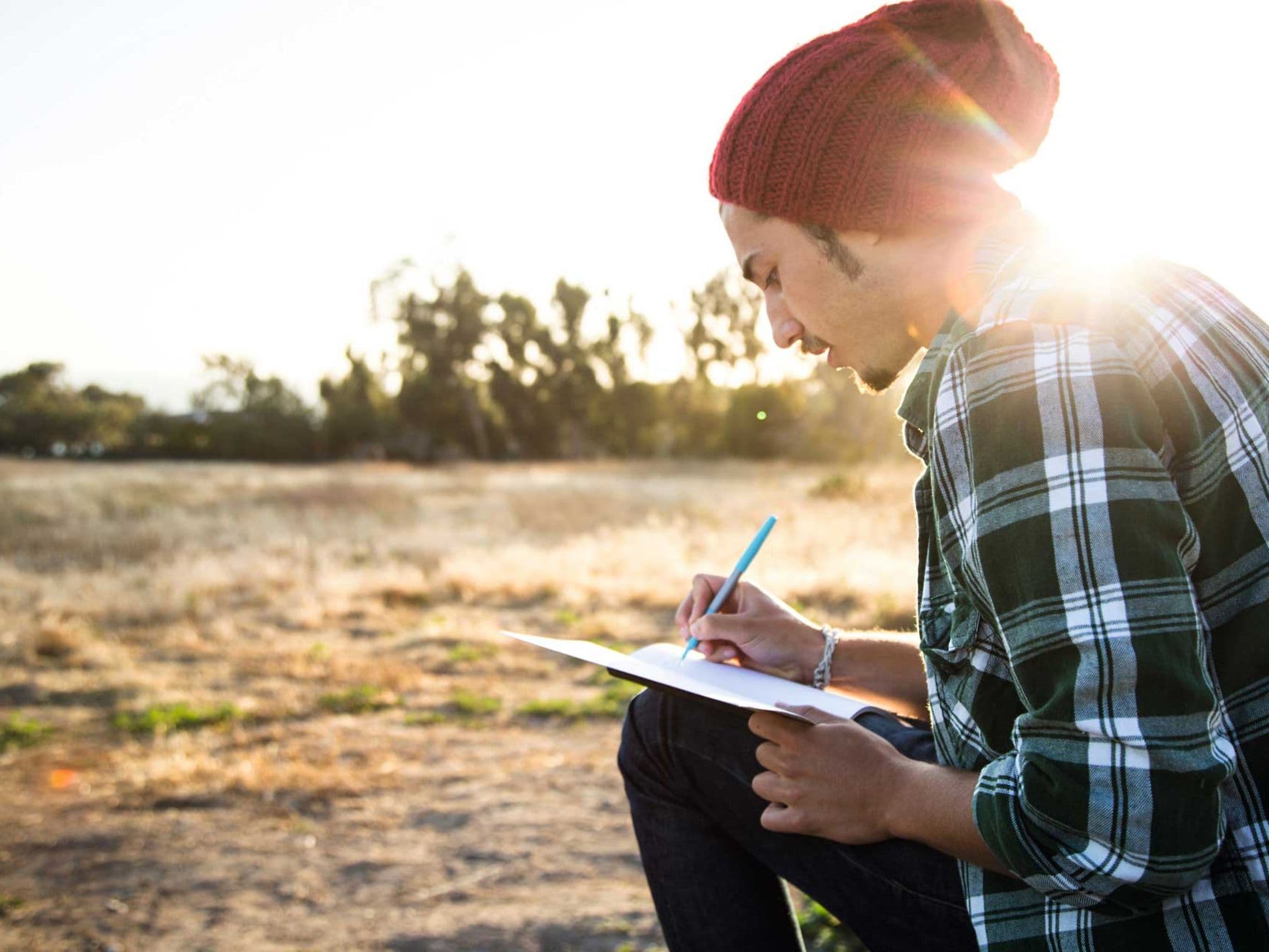 DAK Campus-Planer: Student schreibt Notizen in den Planer draußen auf einer Wiese.
