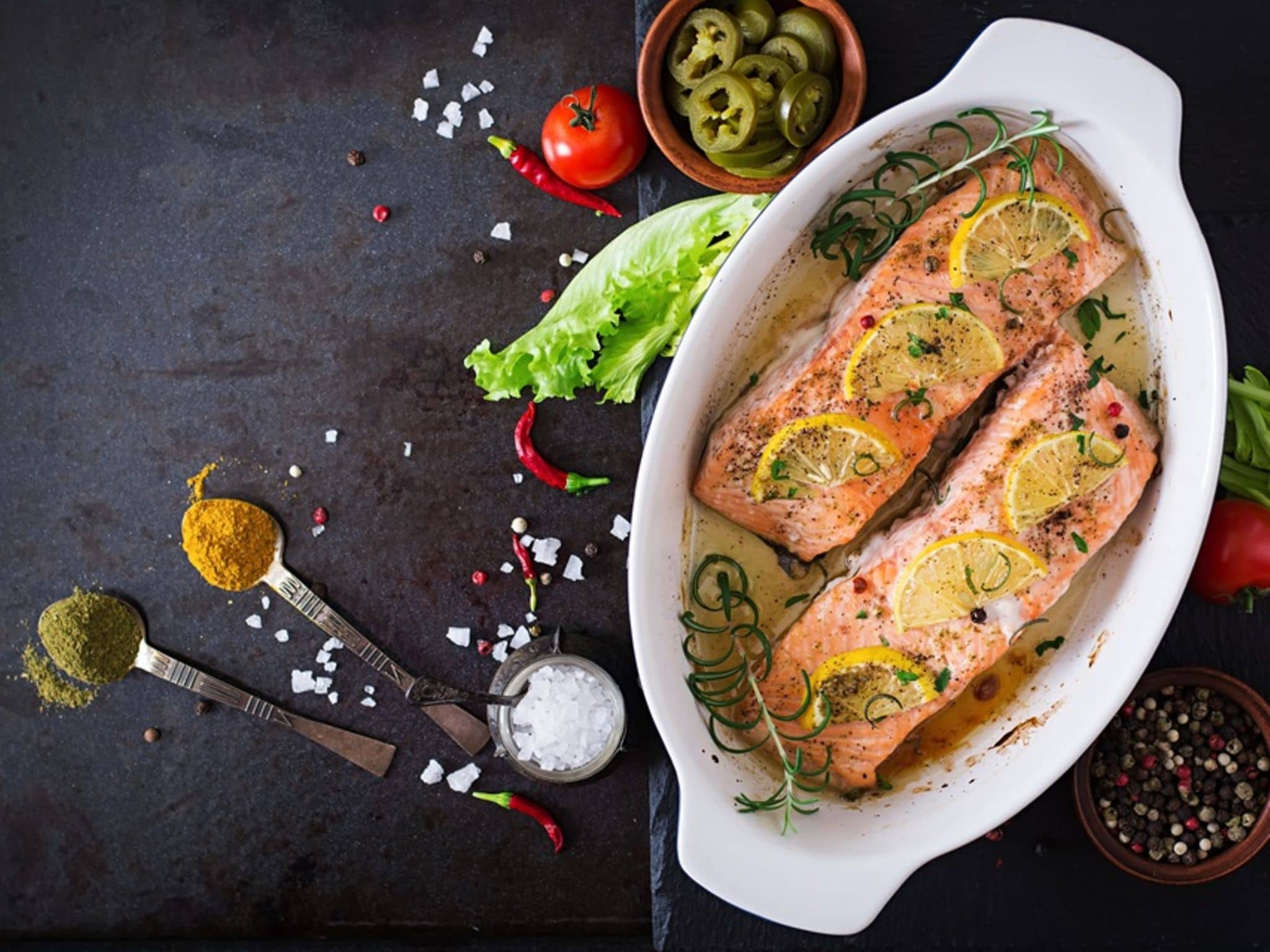 Überbackener Lachs in einer Auflaufform garniert mit Zitronenschreiben und Rosmarin.