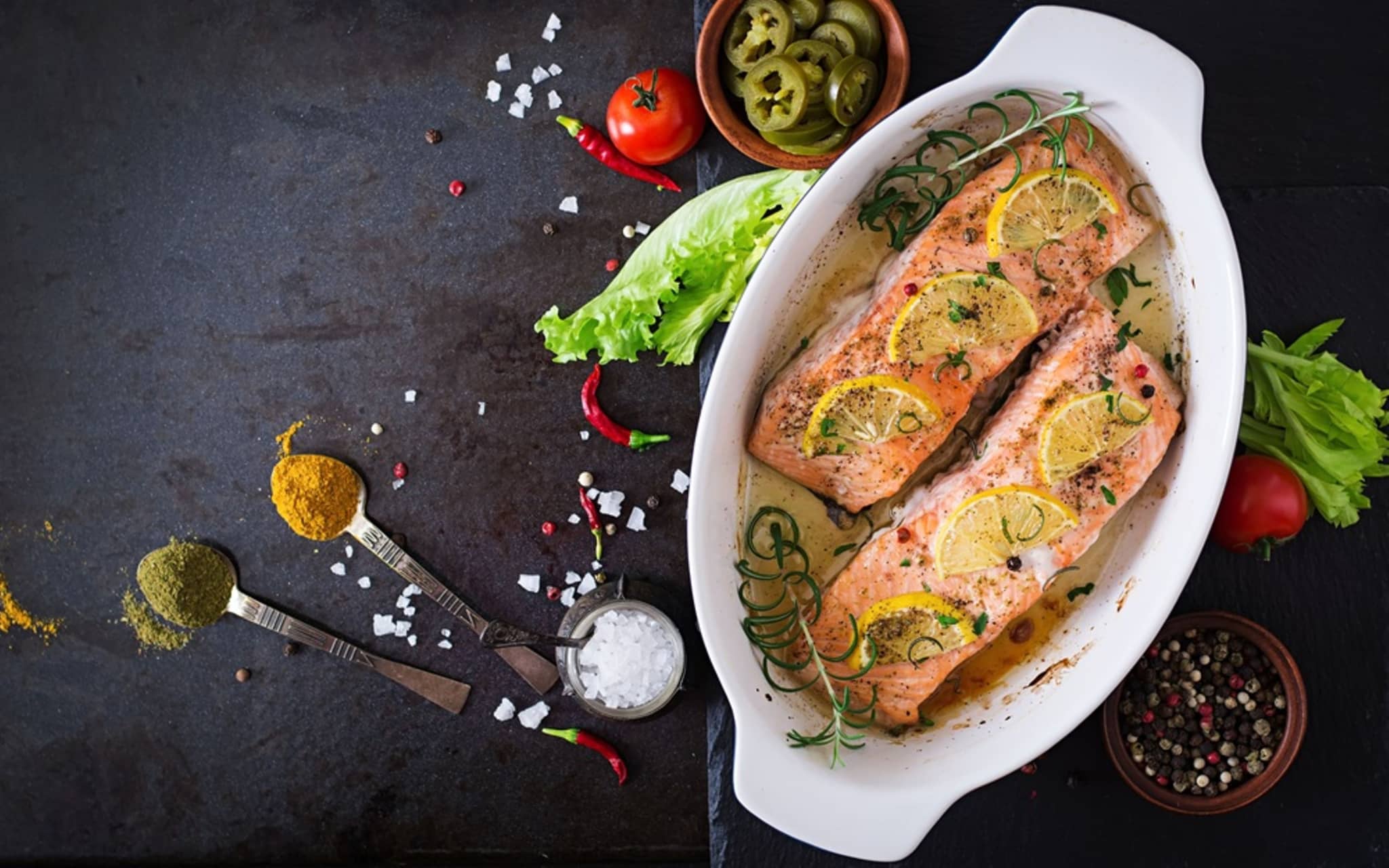 Überbackener Lachs in einer Auflaufform garniert mit Zitronenschreiben und Rosmarin.