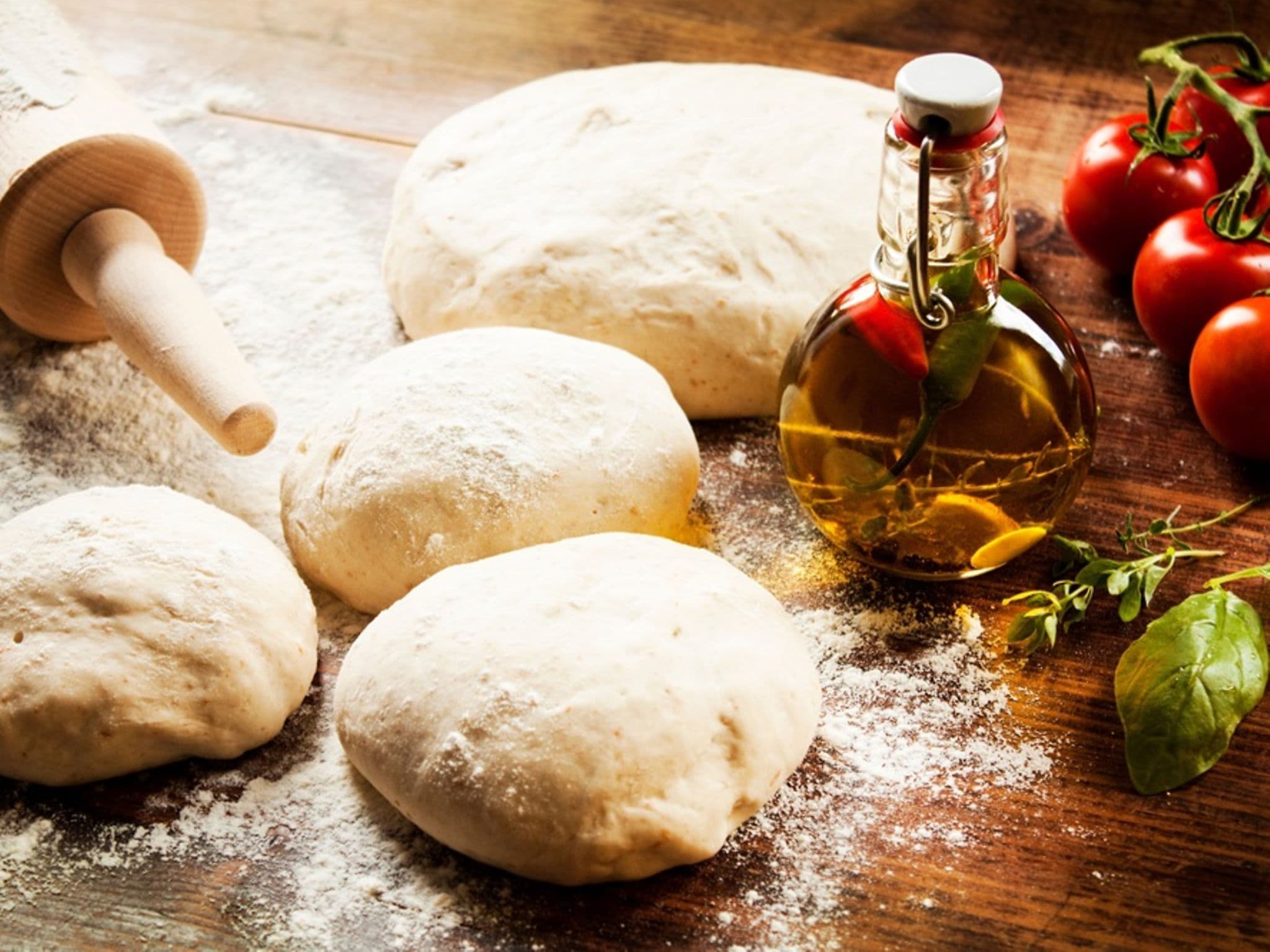 Vier Teigkugeln die bereitliegen, um zum Pizzateig ausgerollt zu werden.