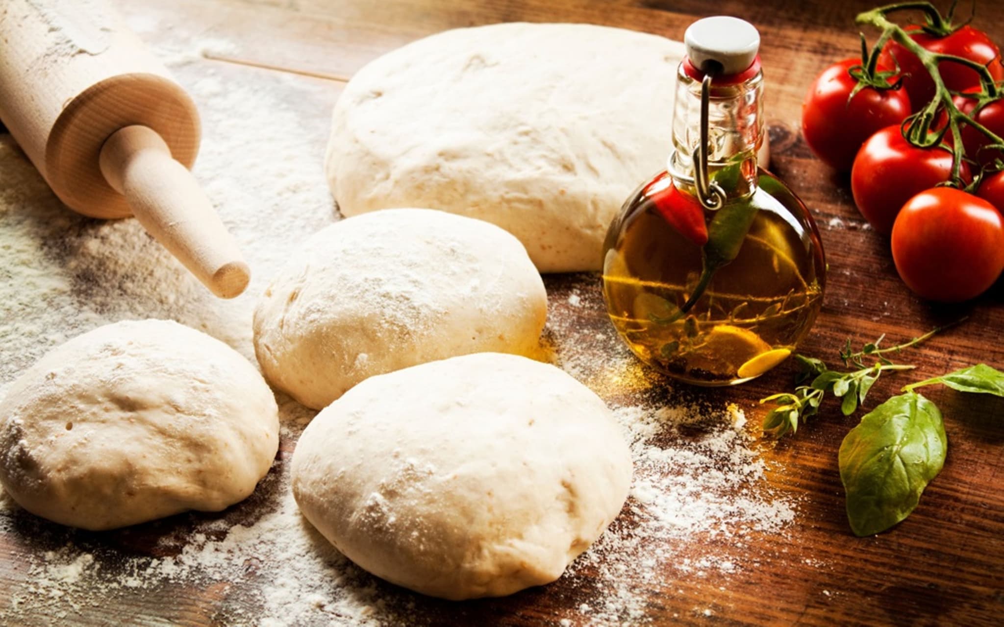 Vier Teigkugeln die bereitliegen, um zum Pizzateig ausgerollt zu werden.