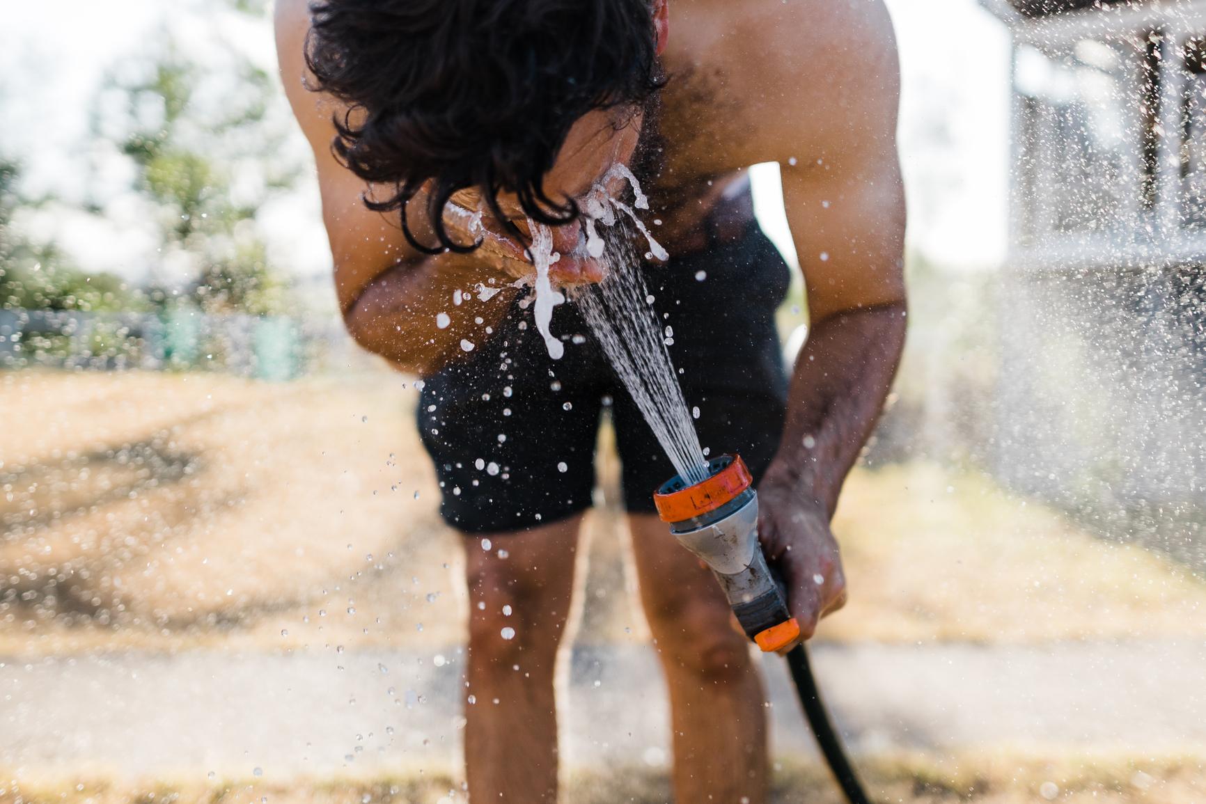 Dehydrierung beim Sport: Ein Mann wäscht sich sein Gesicht mit einem Gartenschlauch